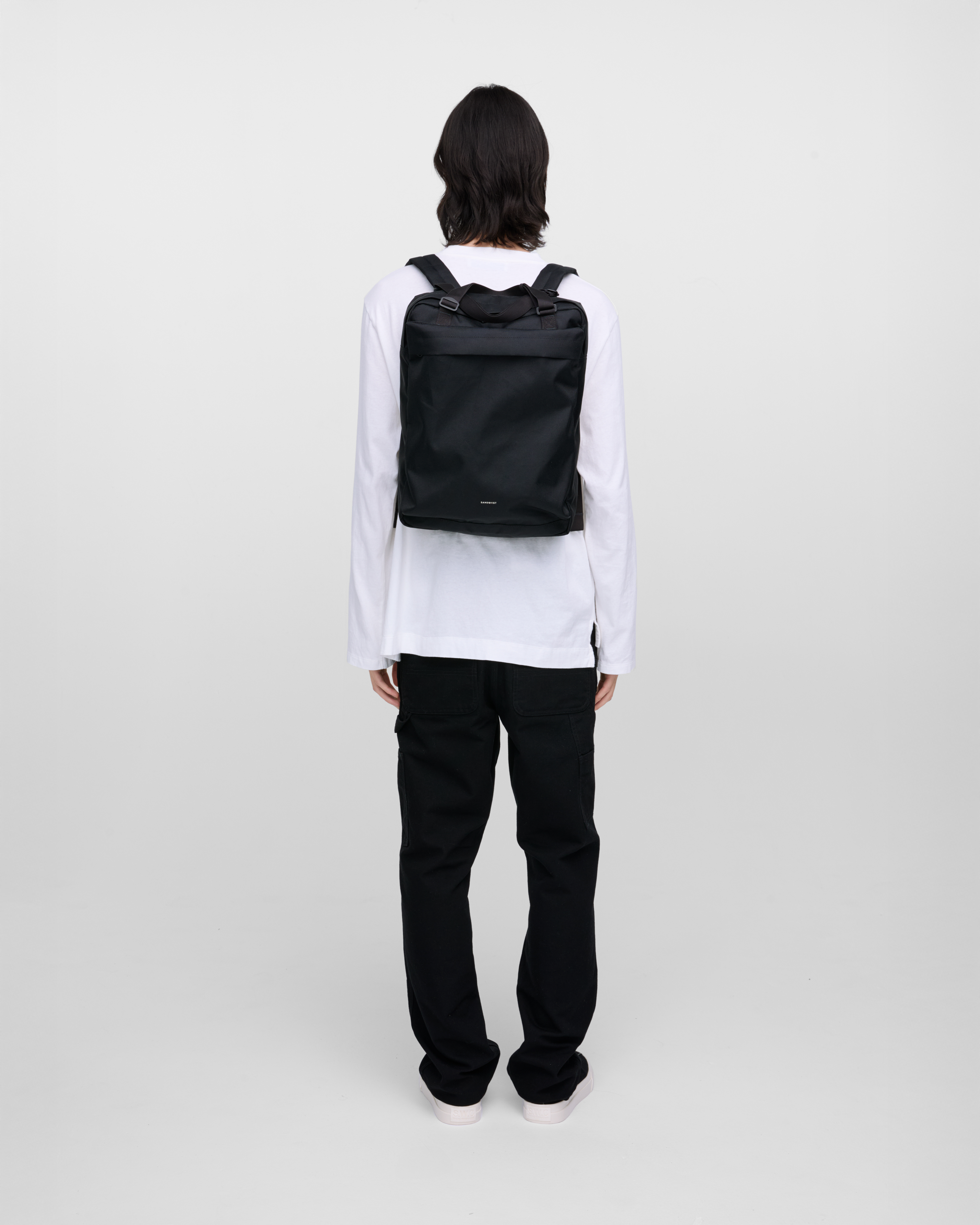 Male model wearing Sandqvist Go 2-way Tote Bag, black. Back view, wearing the bag on the back.