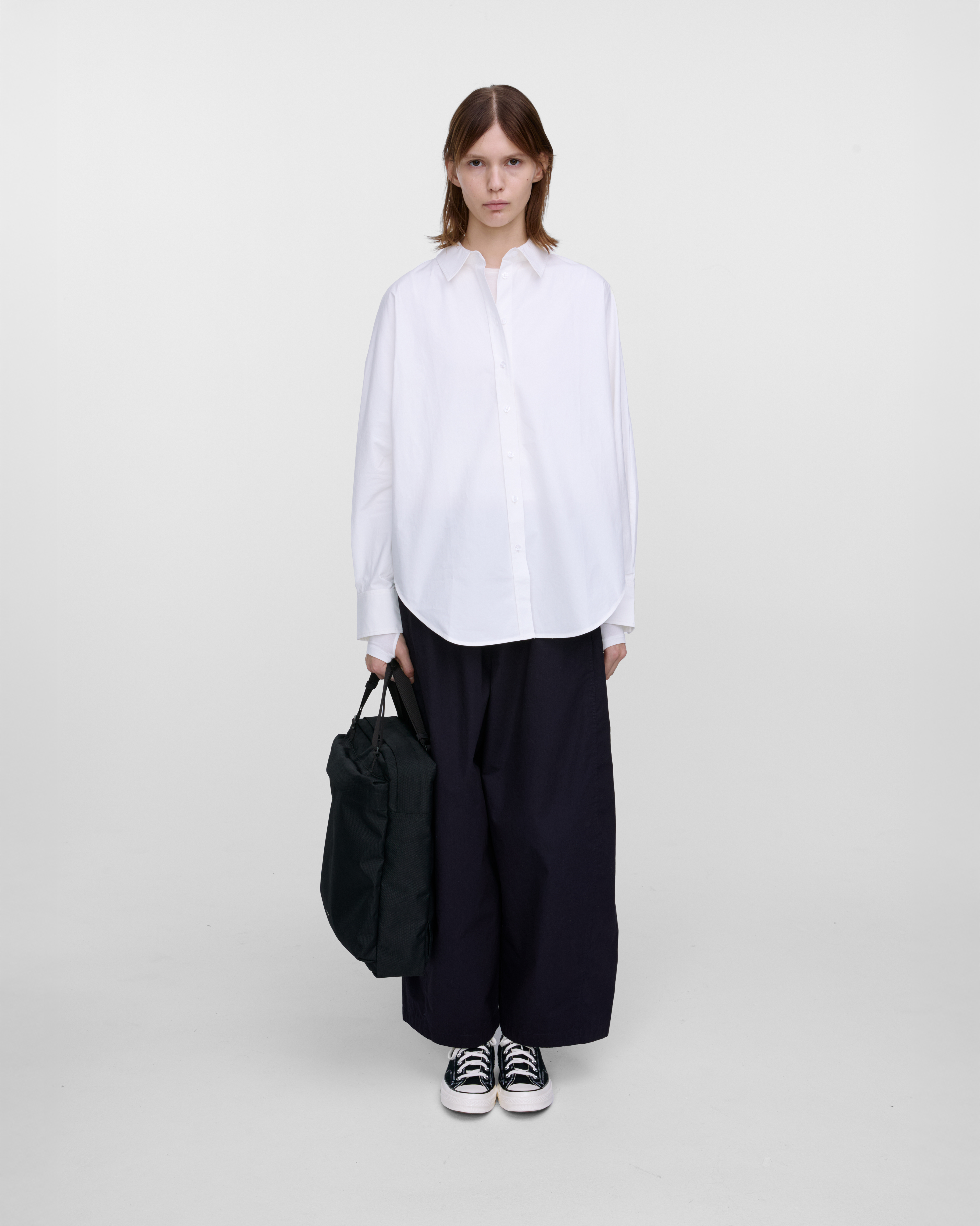 Female model holding Sandqvist Go 2-way Tote Bag, black. Front view, holding the bag in one hand.