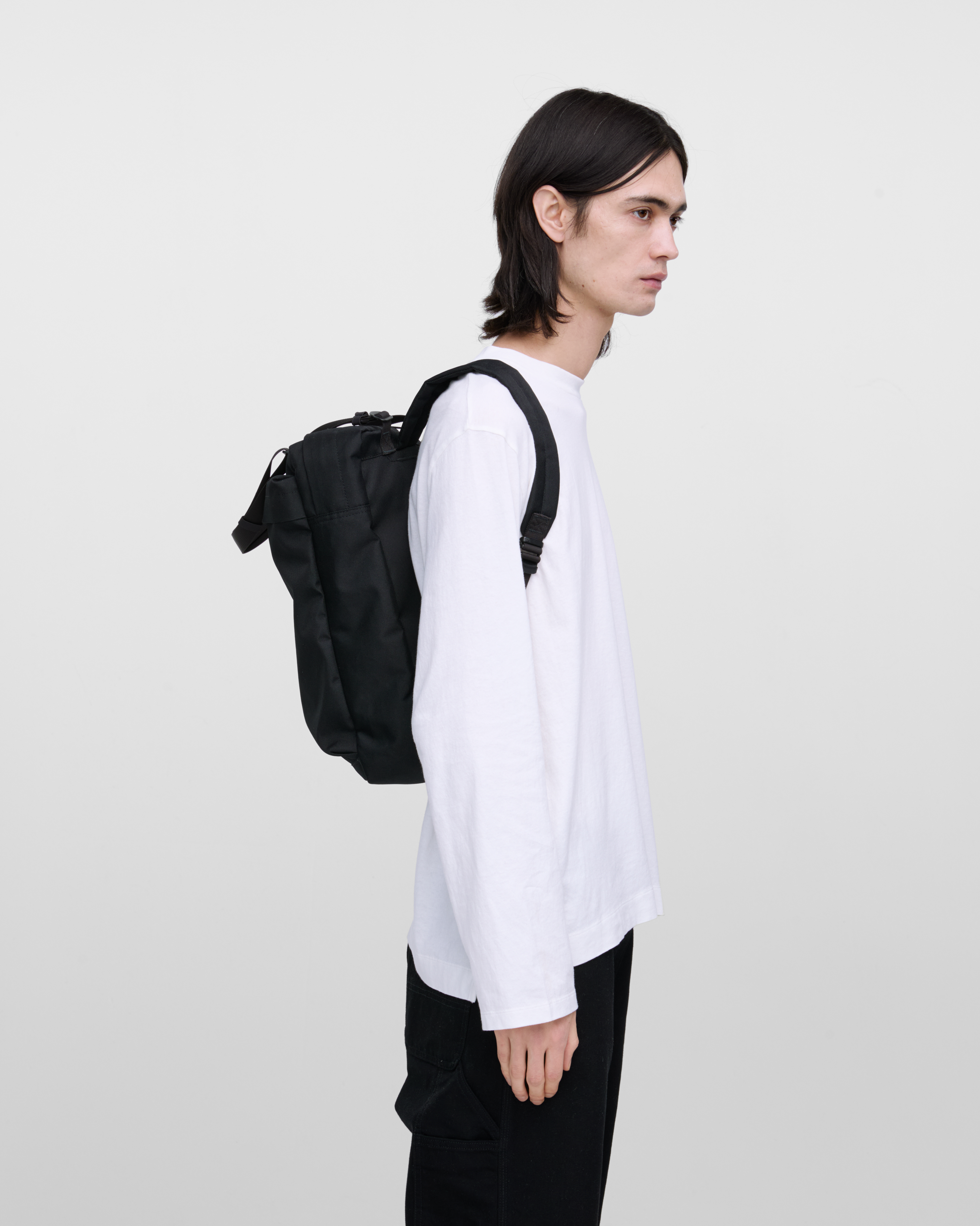 Male model wearing Sandqvist Go 2-way Tote Bag, black. Side view, wearing the bag on the back.