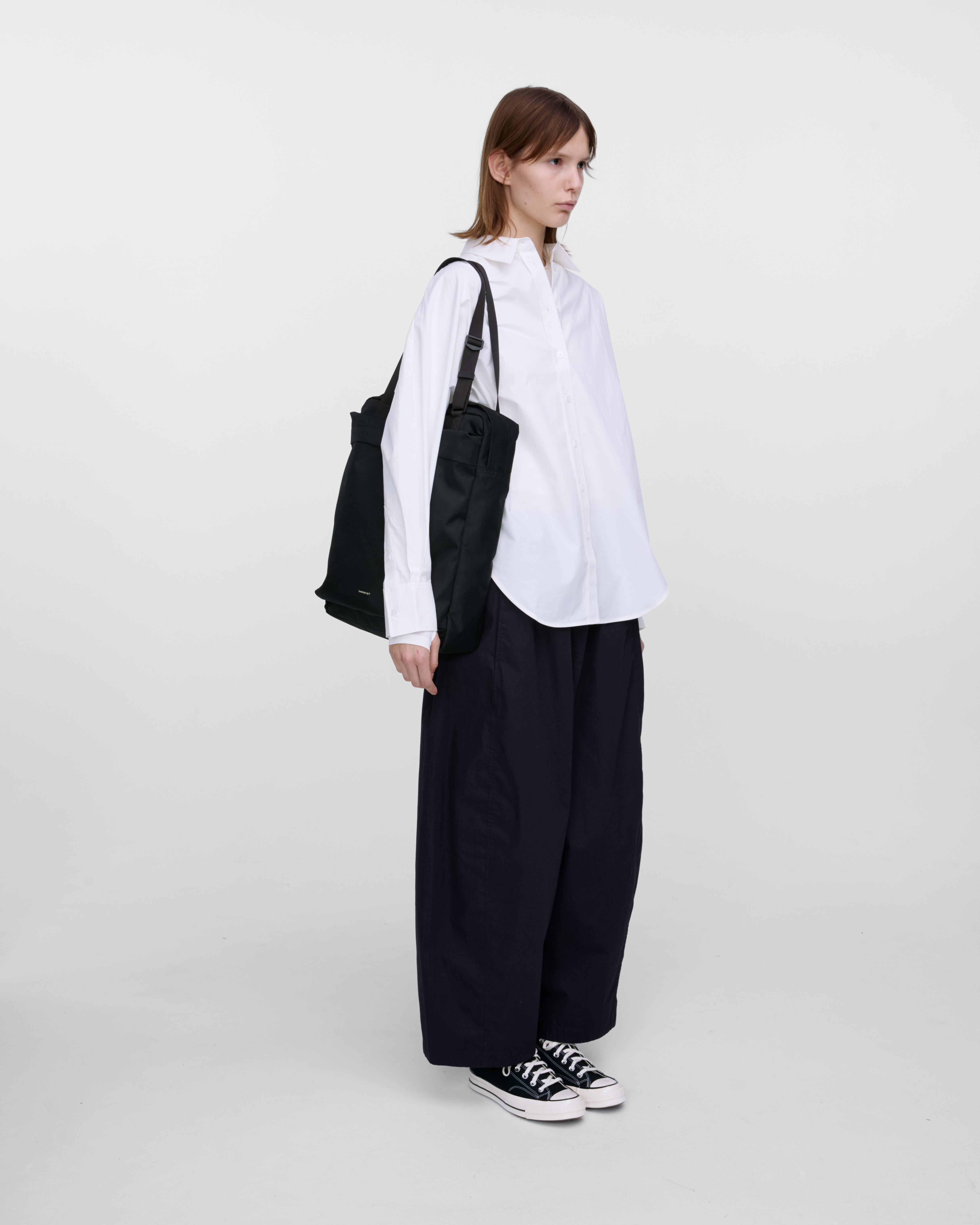 Female model wearing Sandqvist Go 2-way Tote Bag, black. Front view, wearing the bag on one shoulder as a tote bag.