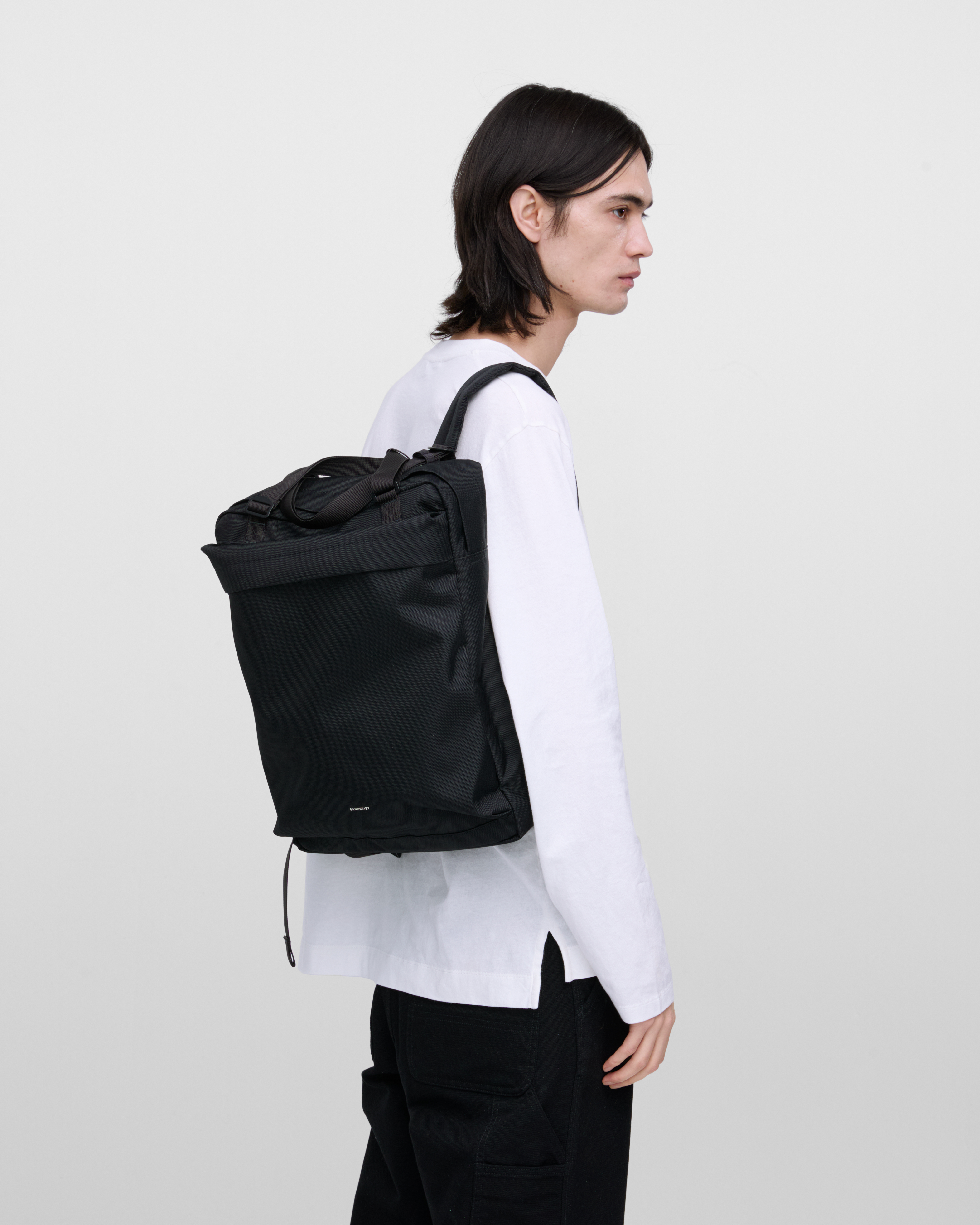Male model wearing Sandqvist Go 2-way Tote Bag, black. Back view, wearing the bag on one shoulder on the back.