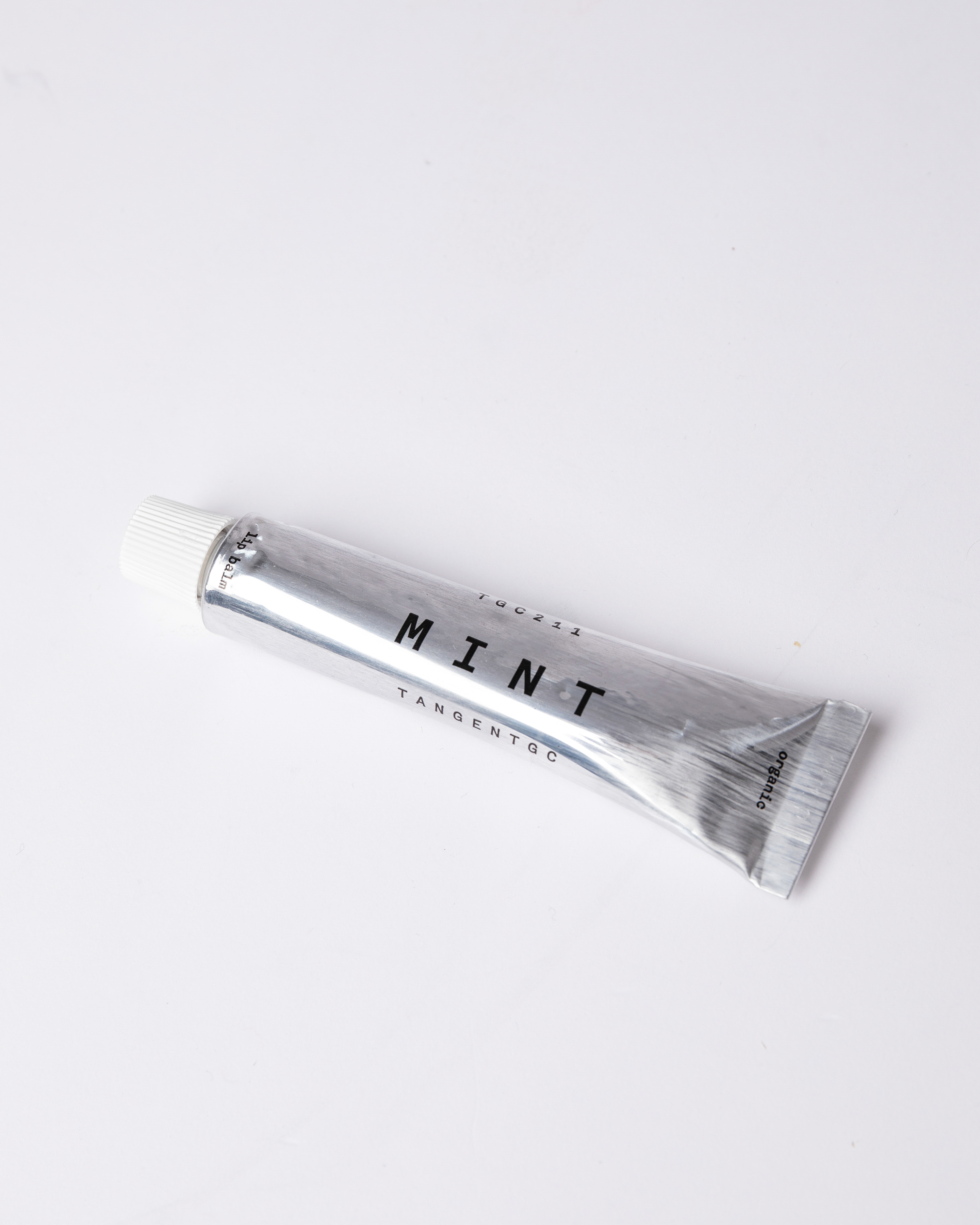 Lip balm in silver tube with white lid. top view showing Sandqvist Mint lip balm laying on flat surface.
