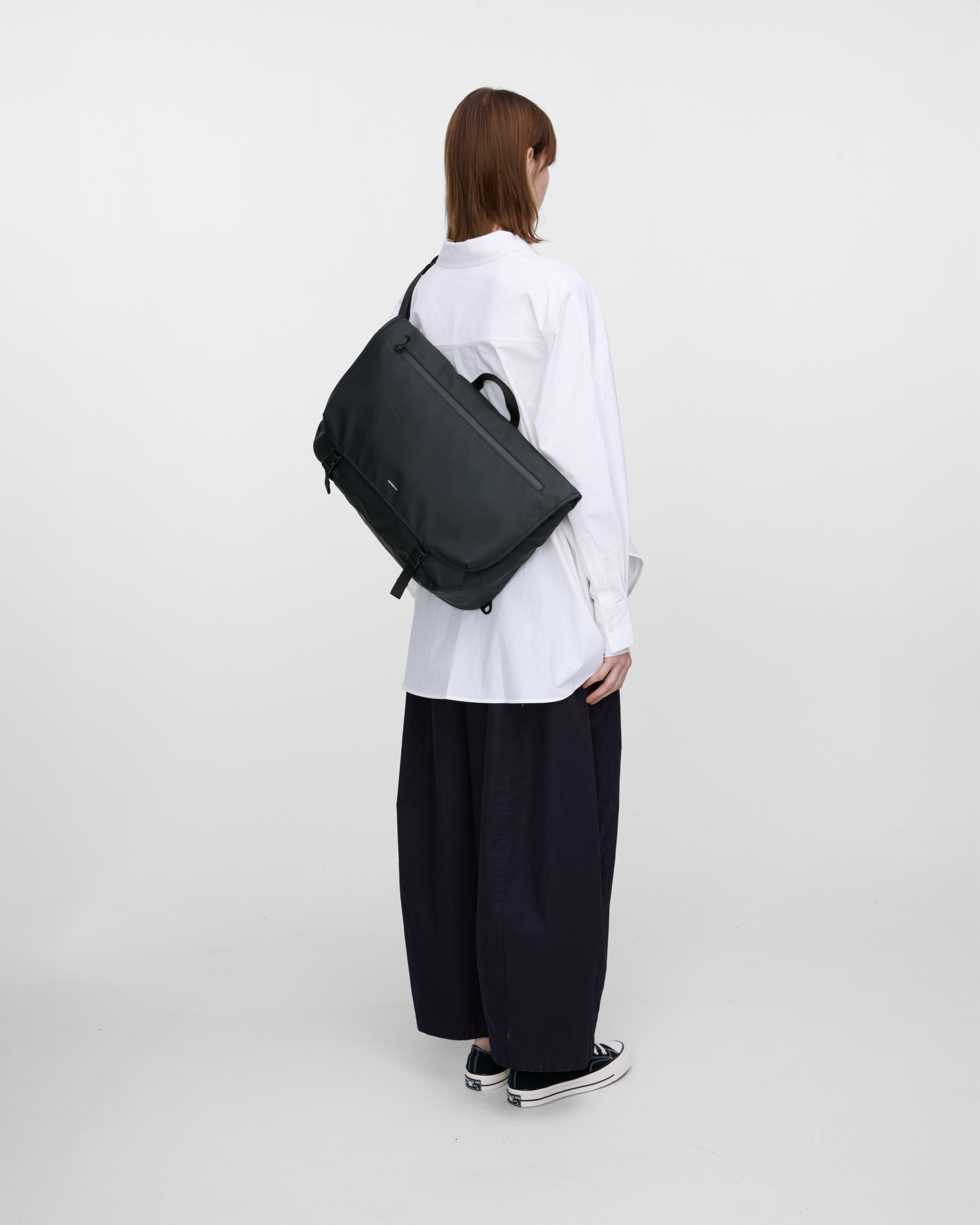 Female model carrying Sandqvist STREAM Messenger Bag in Black on the left shoulder. Back view showing fit and size.