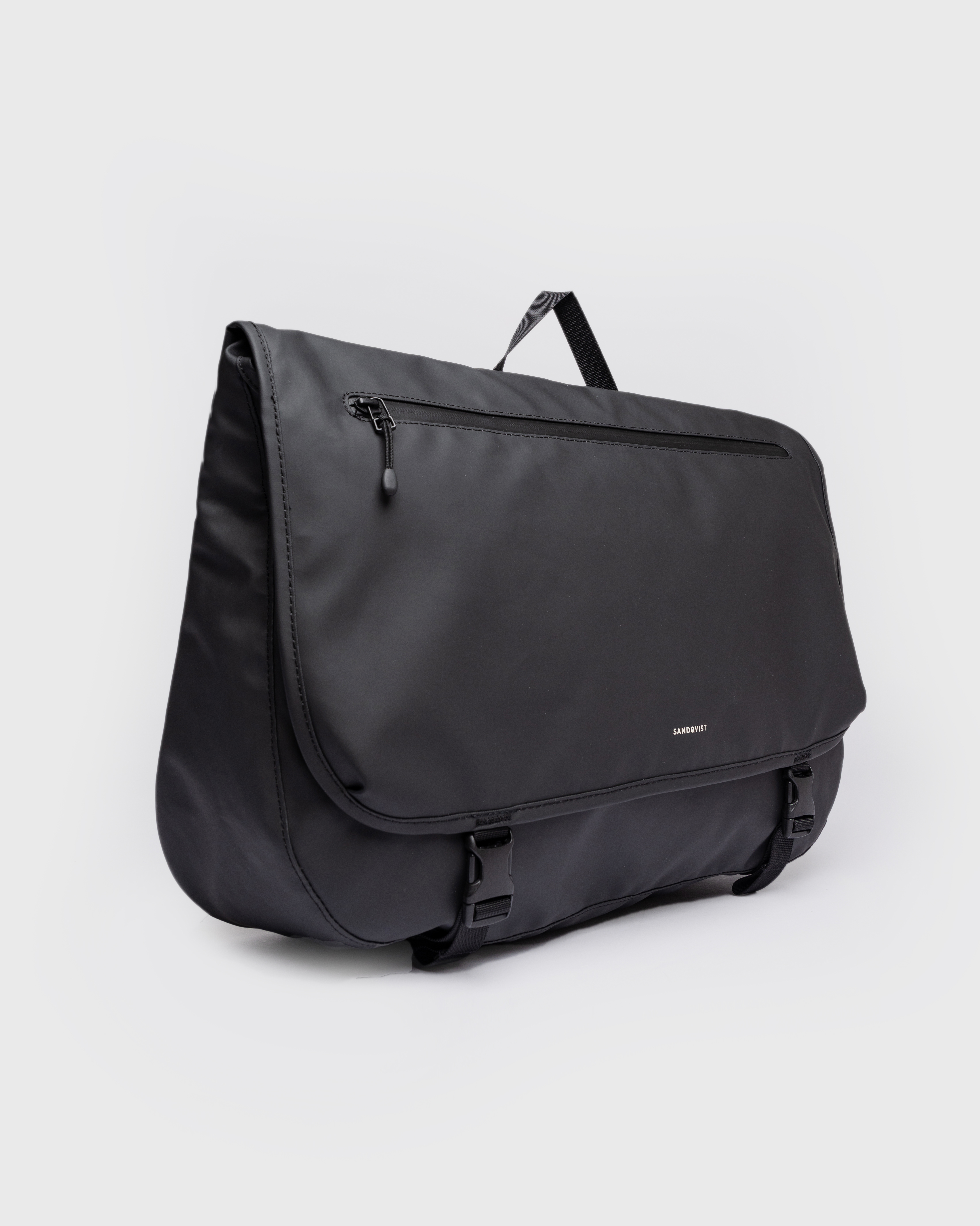 Messenger bag. Sandqvist STREAM Messenger Bag in black, side view with top handle, zipper pocket on lid and two buckles for closure of the lid.