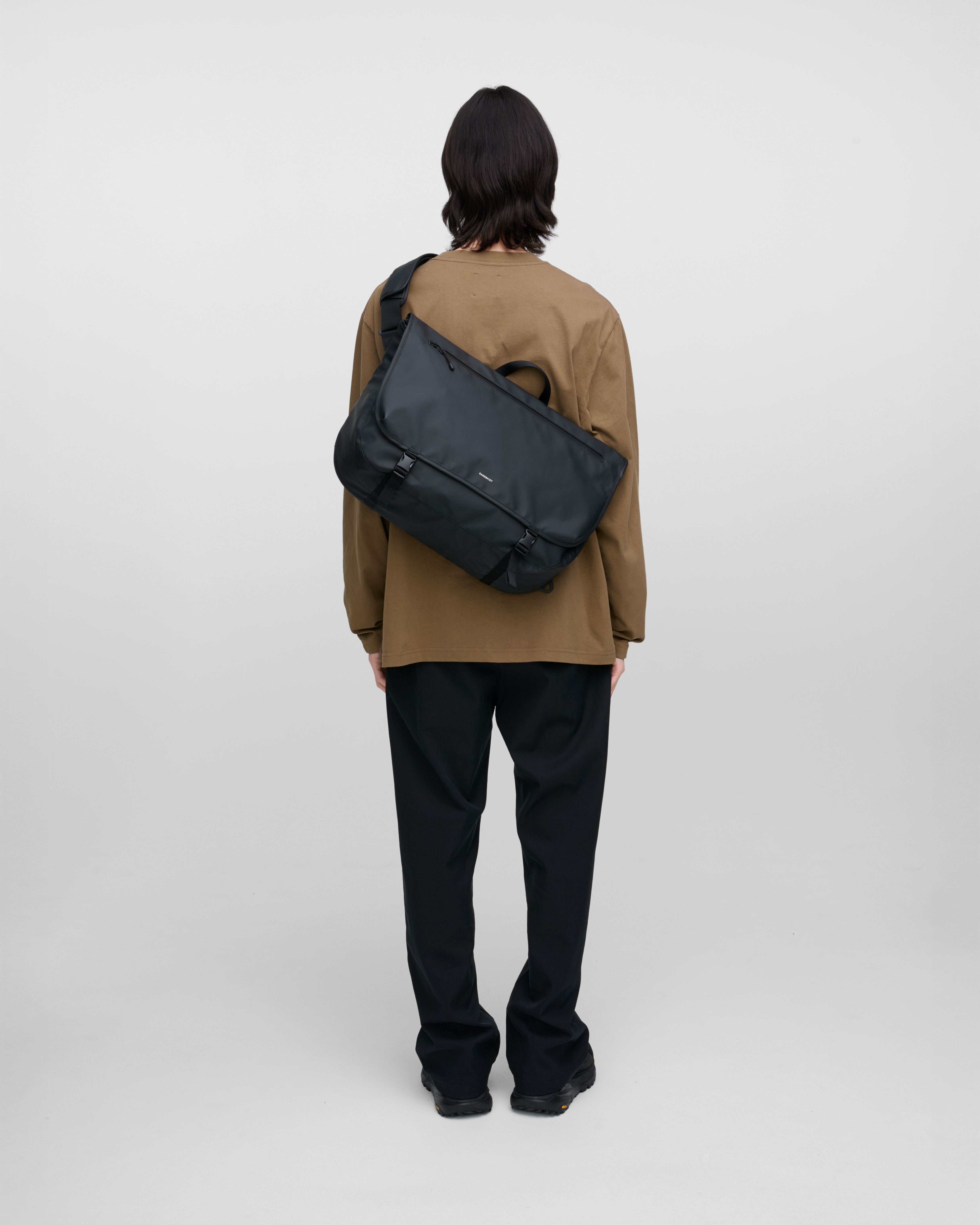 Male model carrying Sandqvist STREAM Messenger Bag in Black on the left shoulder. Back view showing fit and size.