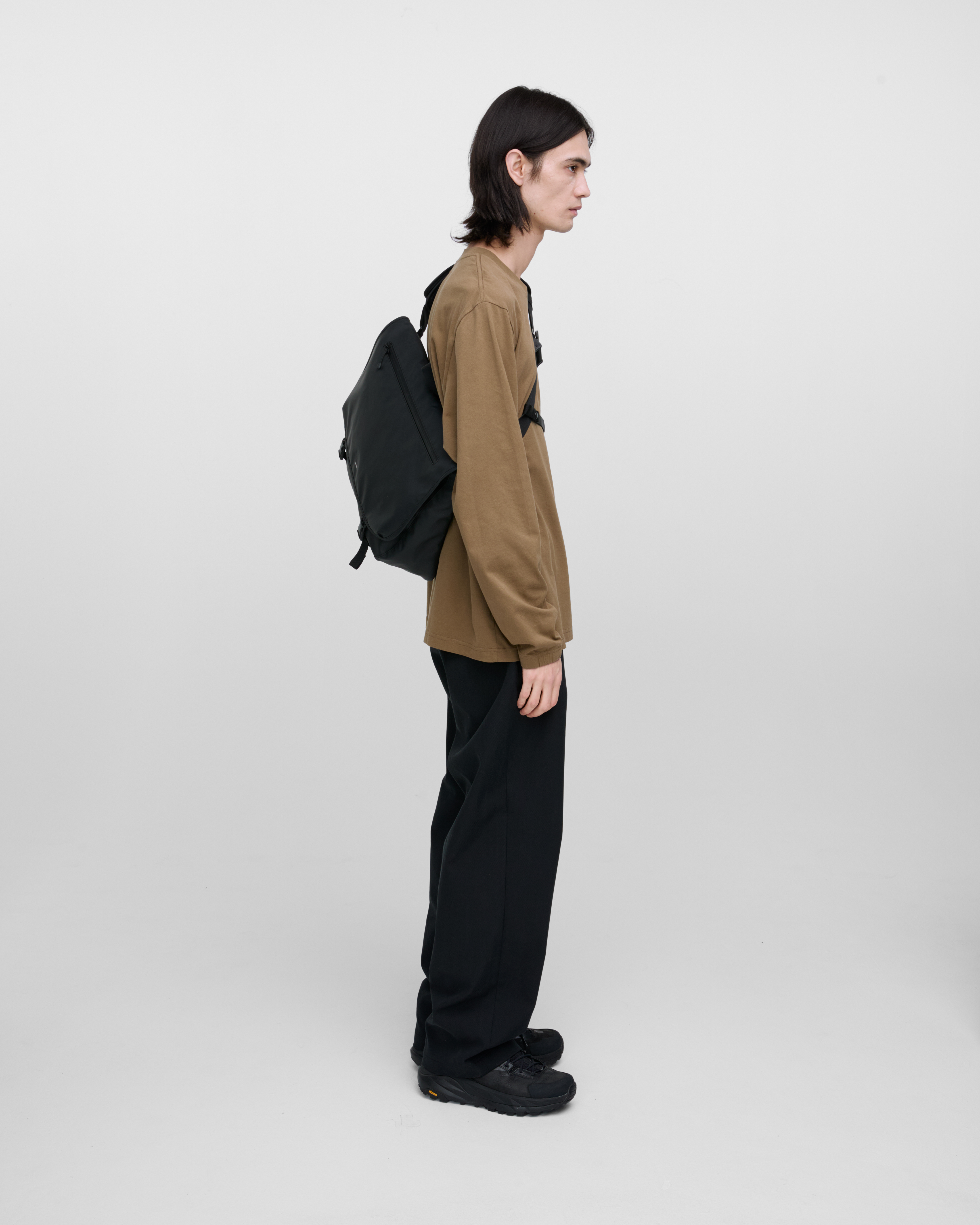 Male model carrying Sandqvist STREAM Messenger Bag in Black on the left shoulder. Right side view showing fit and size.