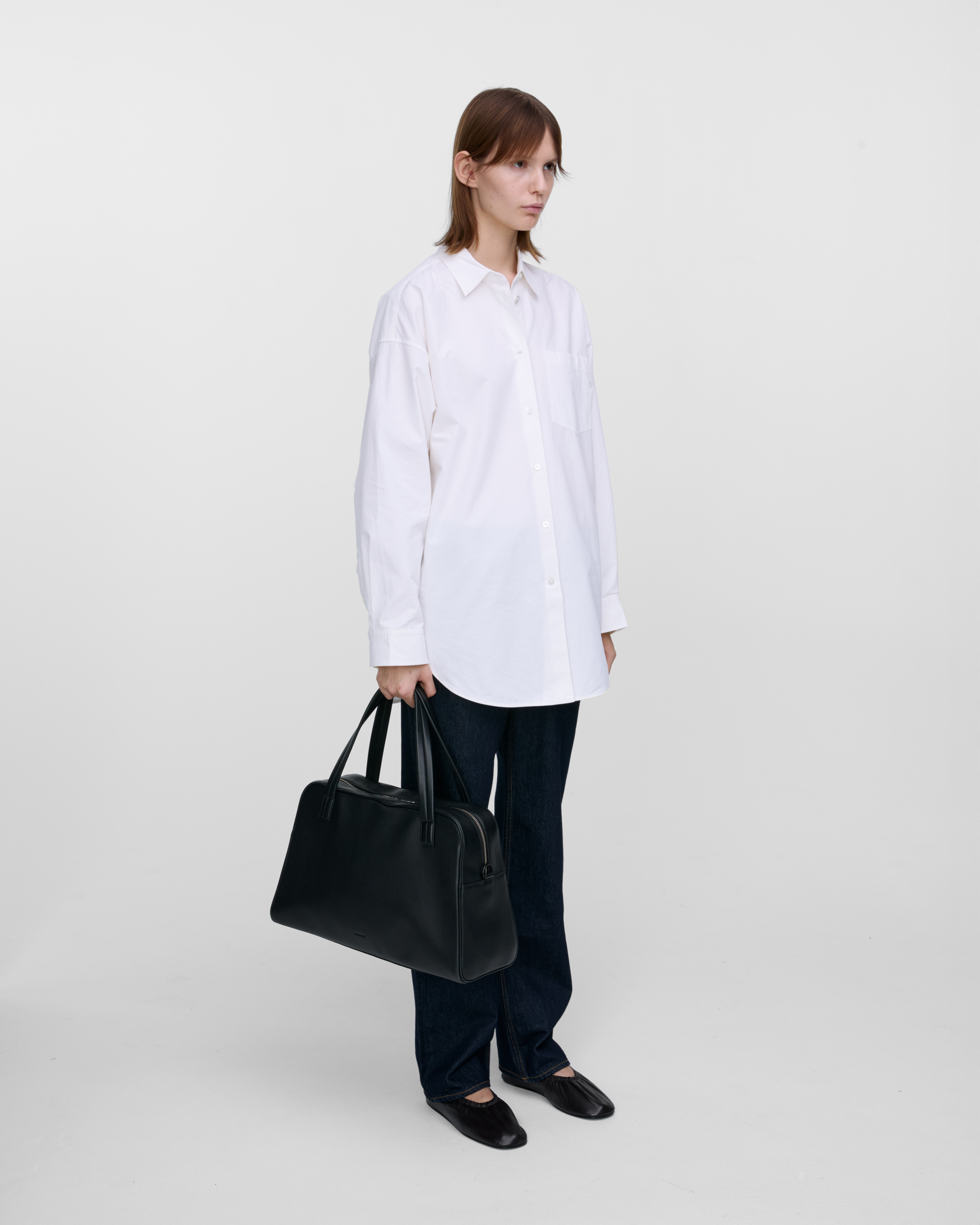 Female model holding the handbag Sandqvist LEATHER Bowling Bag Black in her hand. Side view showing size.