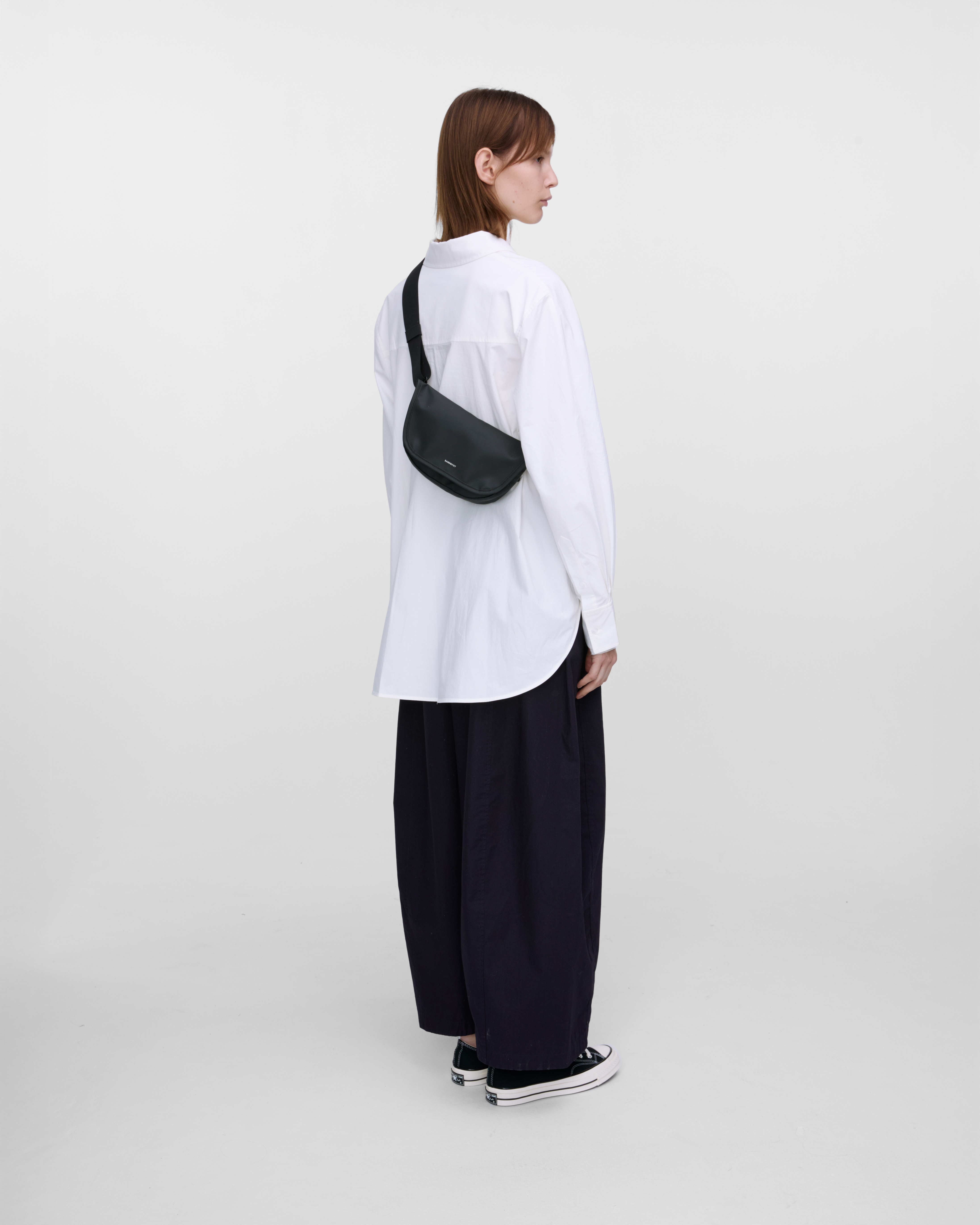 Crossbody bag. Sandqvist STREAM Messenger Mini in black on a female model, back view showing fit and size.