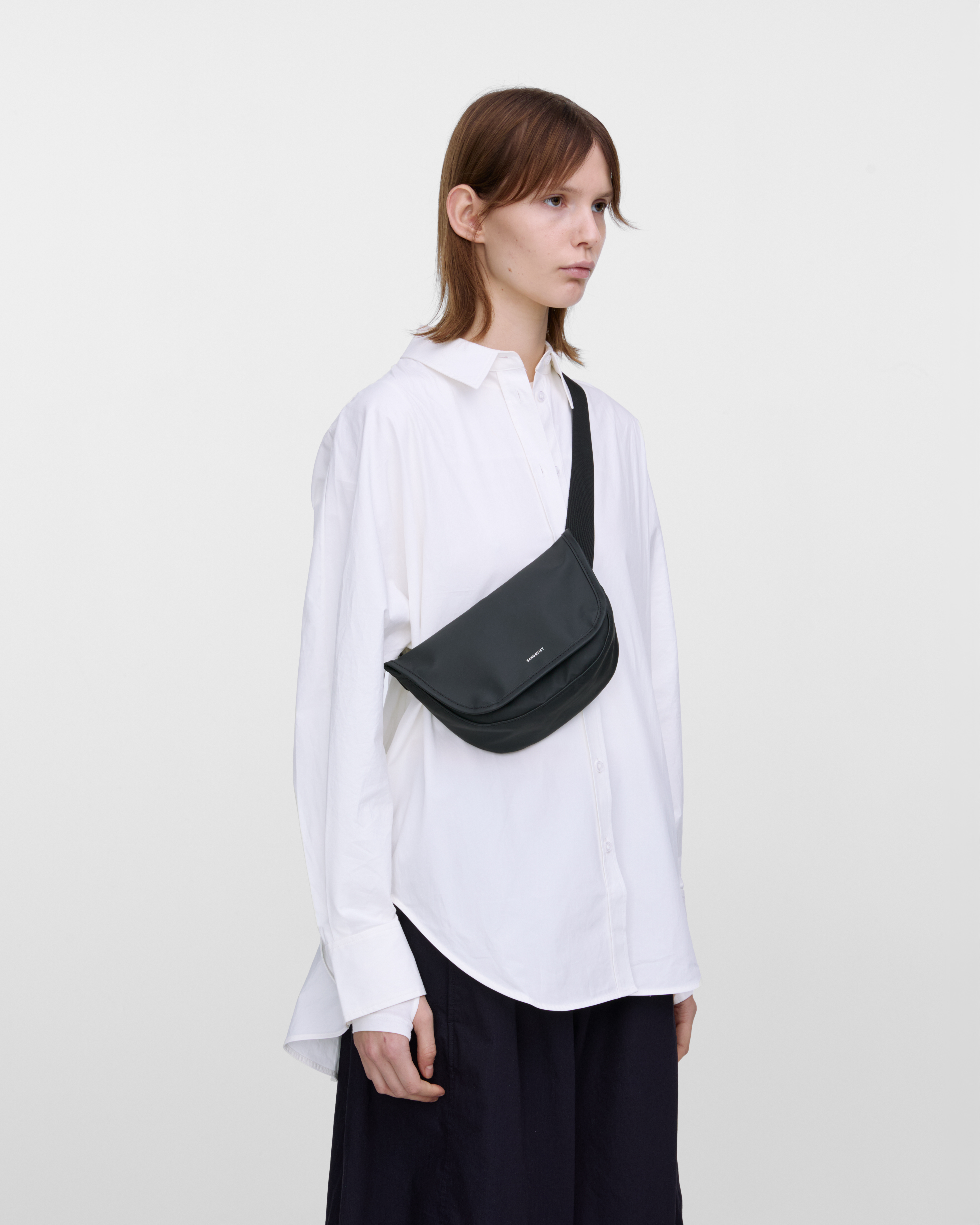 Crossbody bag. Sandqvist STREAM Messenger Mini in black on a female model, front view showing fit and size.