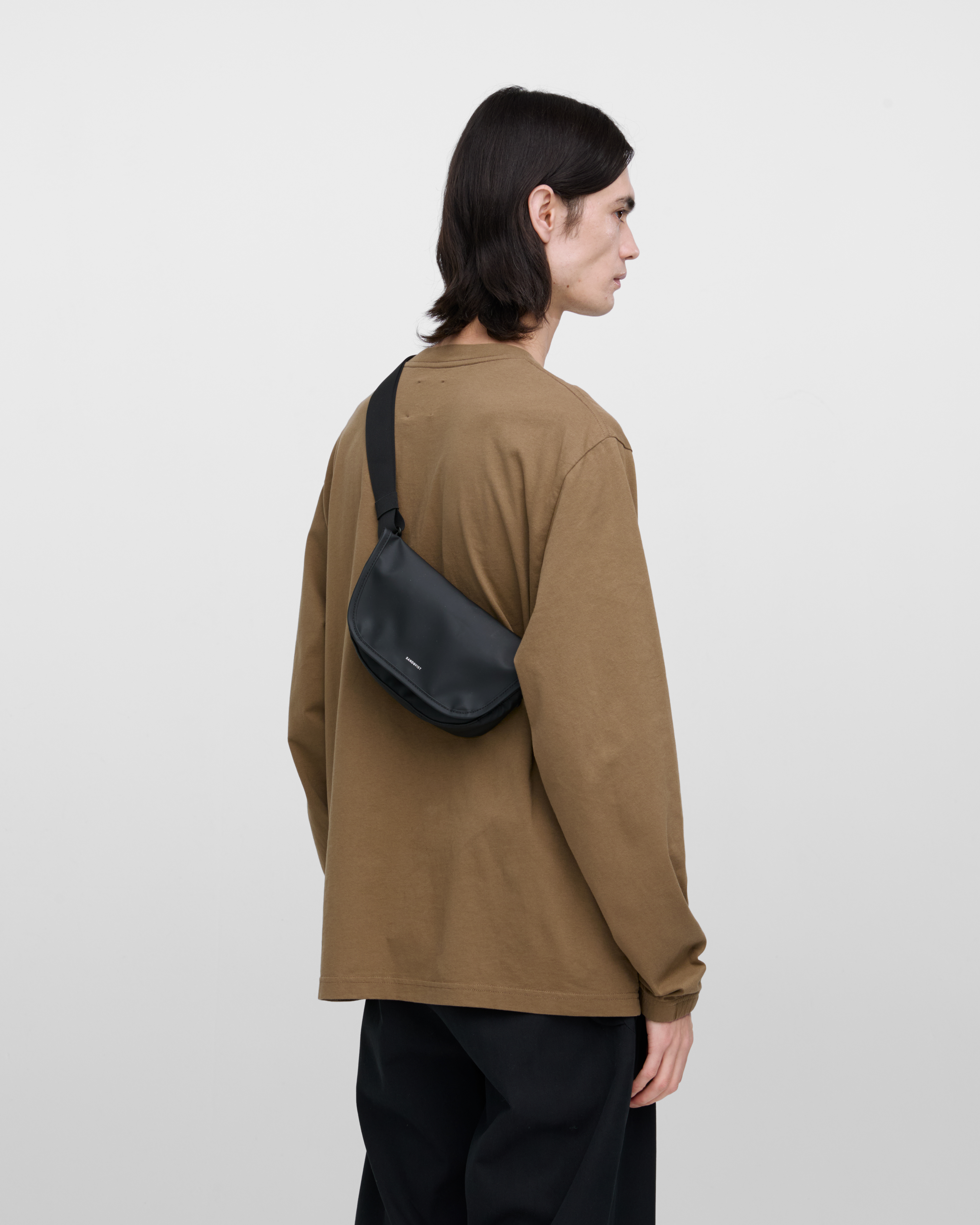 Crossbody bag. Sandqvist STREAM Messenger Mini in black on a male model, back view showing fit and size.