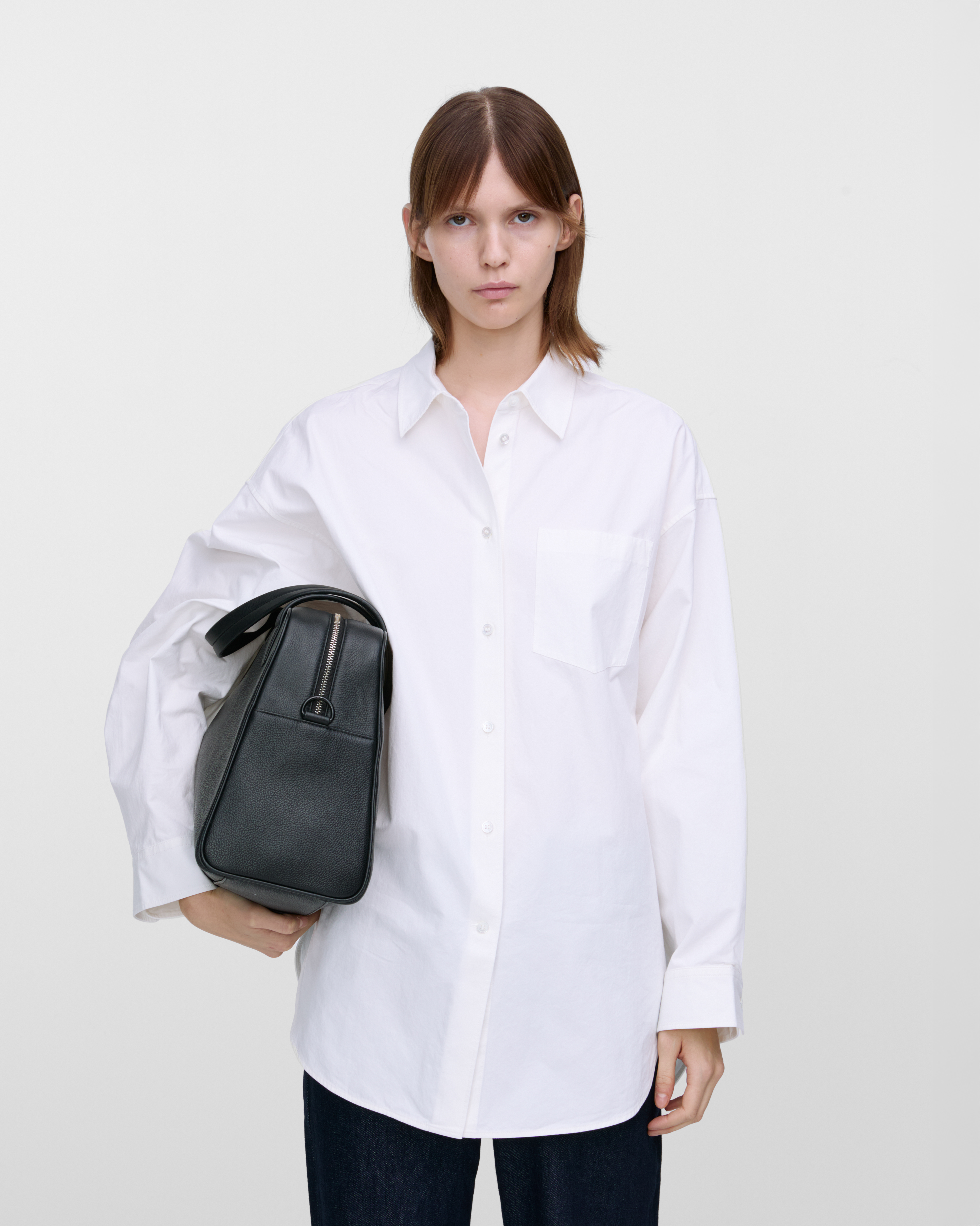 Female model holding the handbag Sandqvist LEATHER Bowling Bag Black under her arm. Front view showing size.
