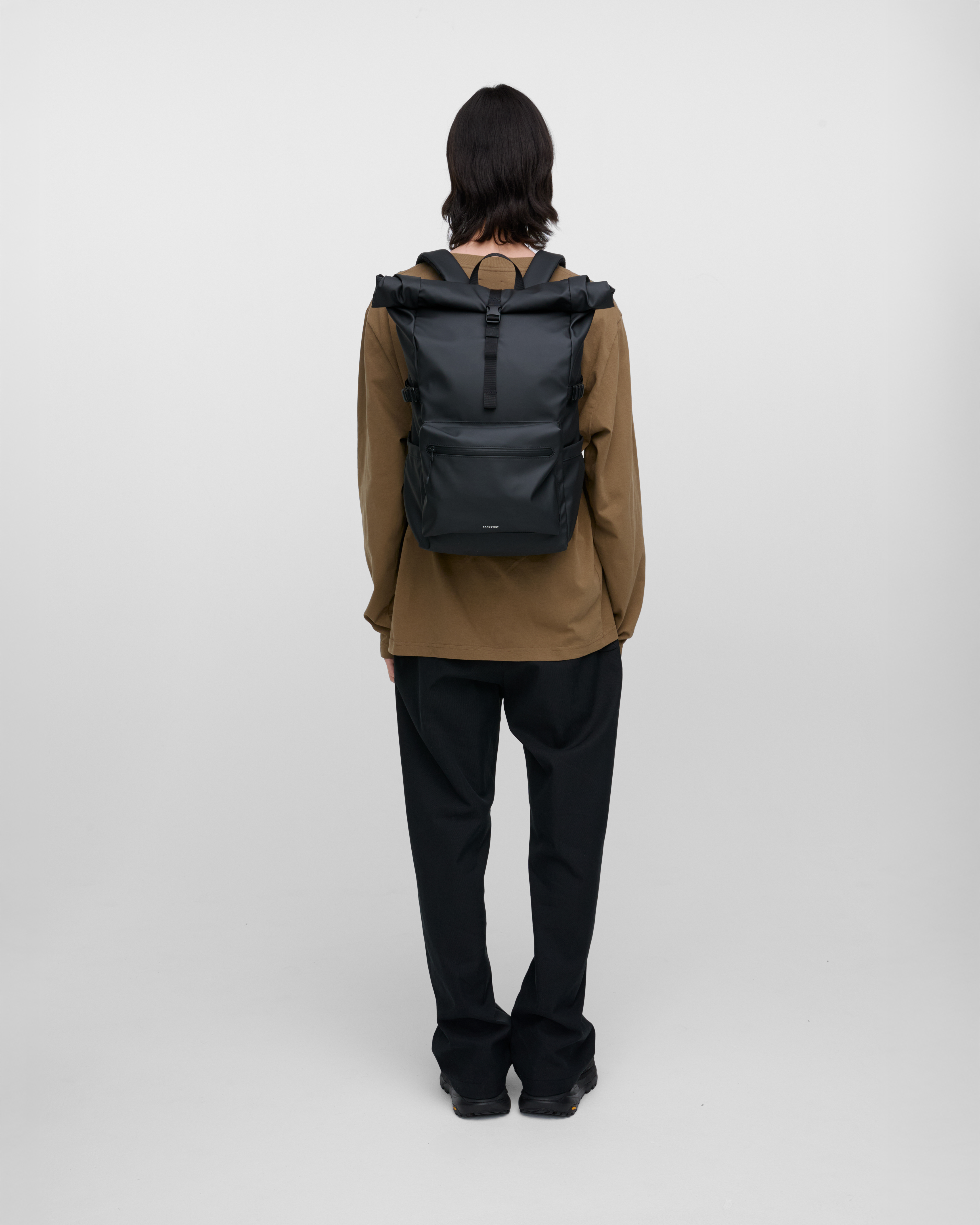 Male model carrying the backpack STREAM Rolltop Backpack L, Black, back view showing fit and size. 