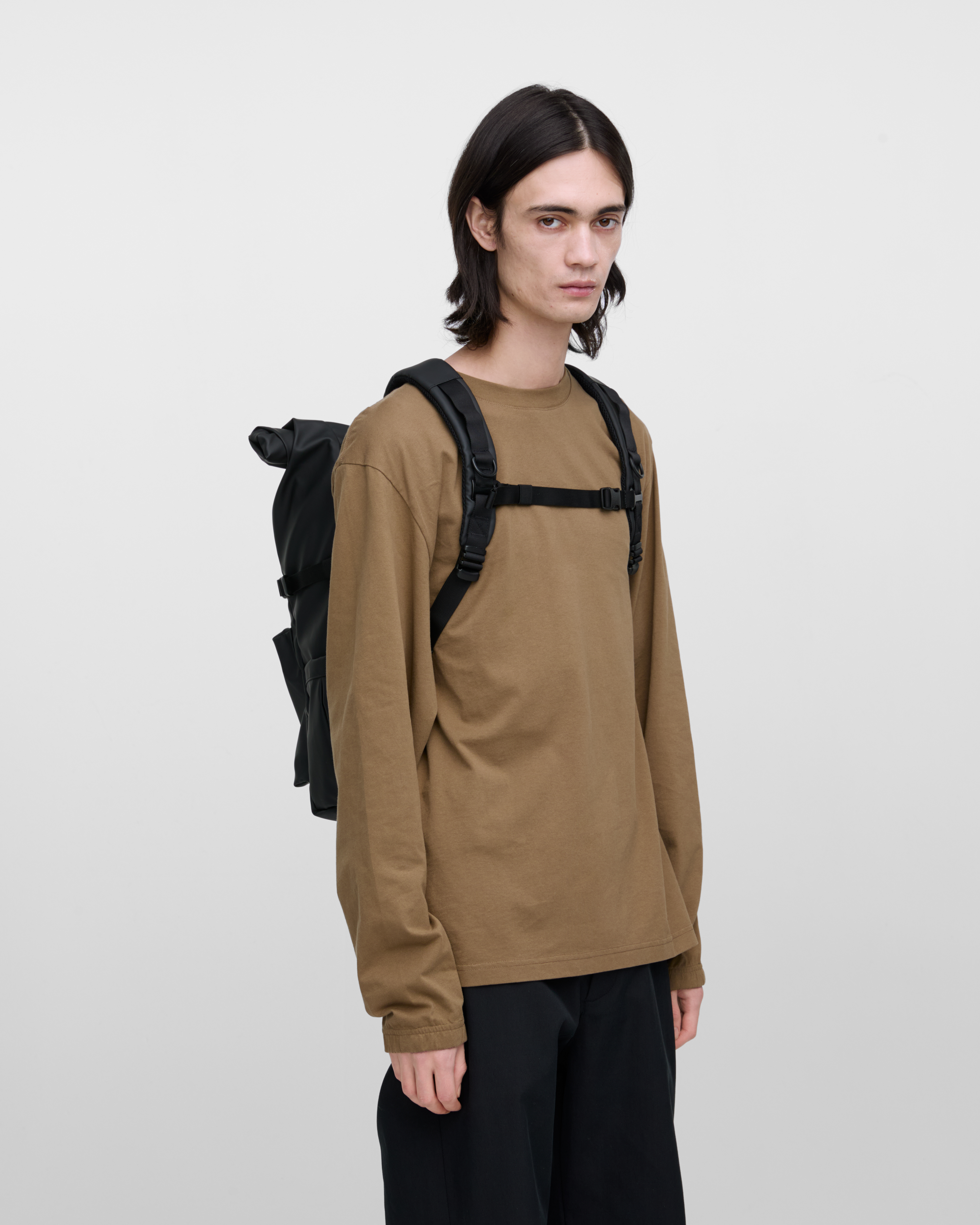 Male model carrying the backpack STREAM Rolltop Backpack L, Black, front view showing fit and size. 