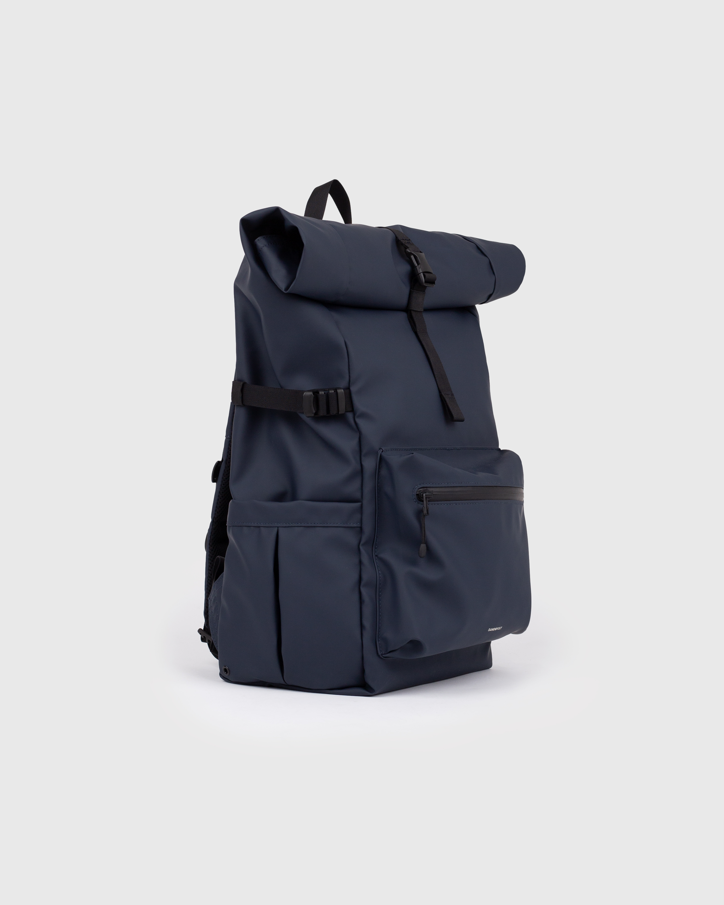 Backpack. Sandqvist STREAM Rolltop Backpack L in dark blue, side view with, top handle, zipper pocket at front, slip pocket, side strap and rolltop closure.