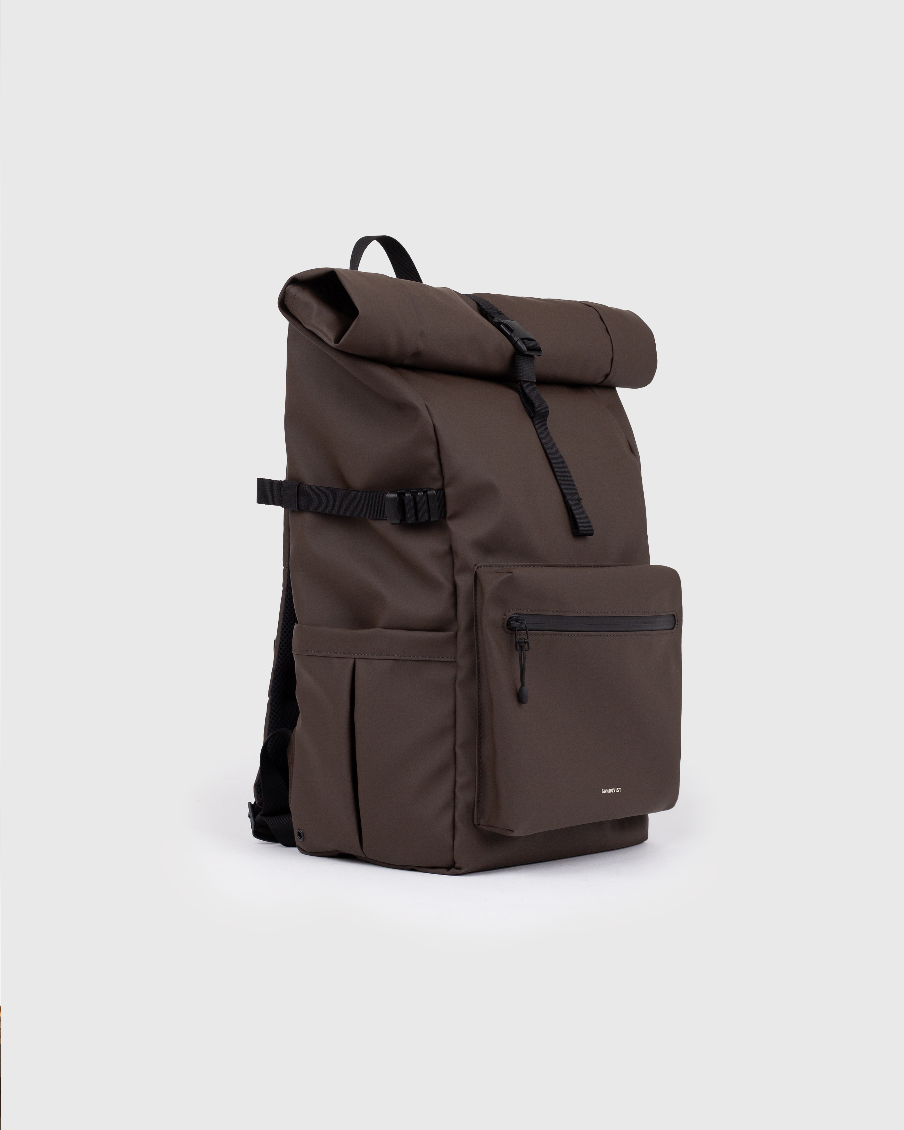Backpack. Sandqvist STREAM Rolltop Backpack L in dark brown, side view with, top handle, zipper pocket at front, slip pocket, side strap and rolltop closure.