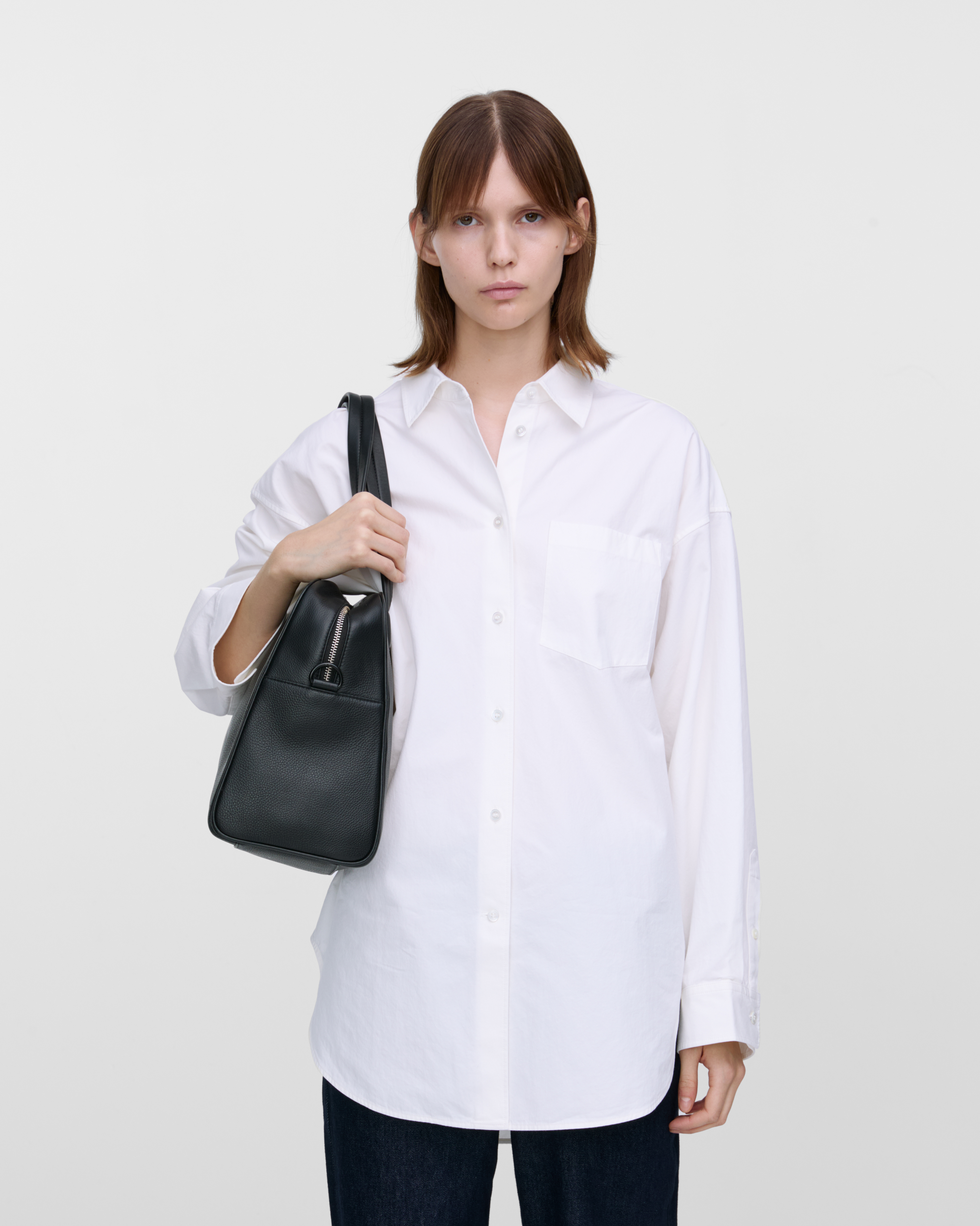 Female model carrying the handbag Sandqvist LEATHER Bowling Bag Black on the shoulder. Front view showing fit and size.