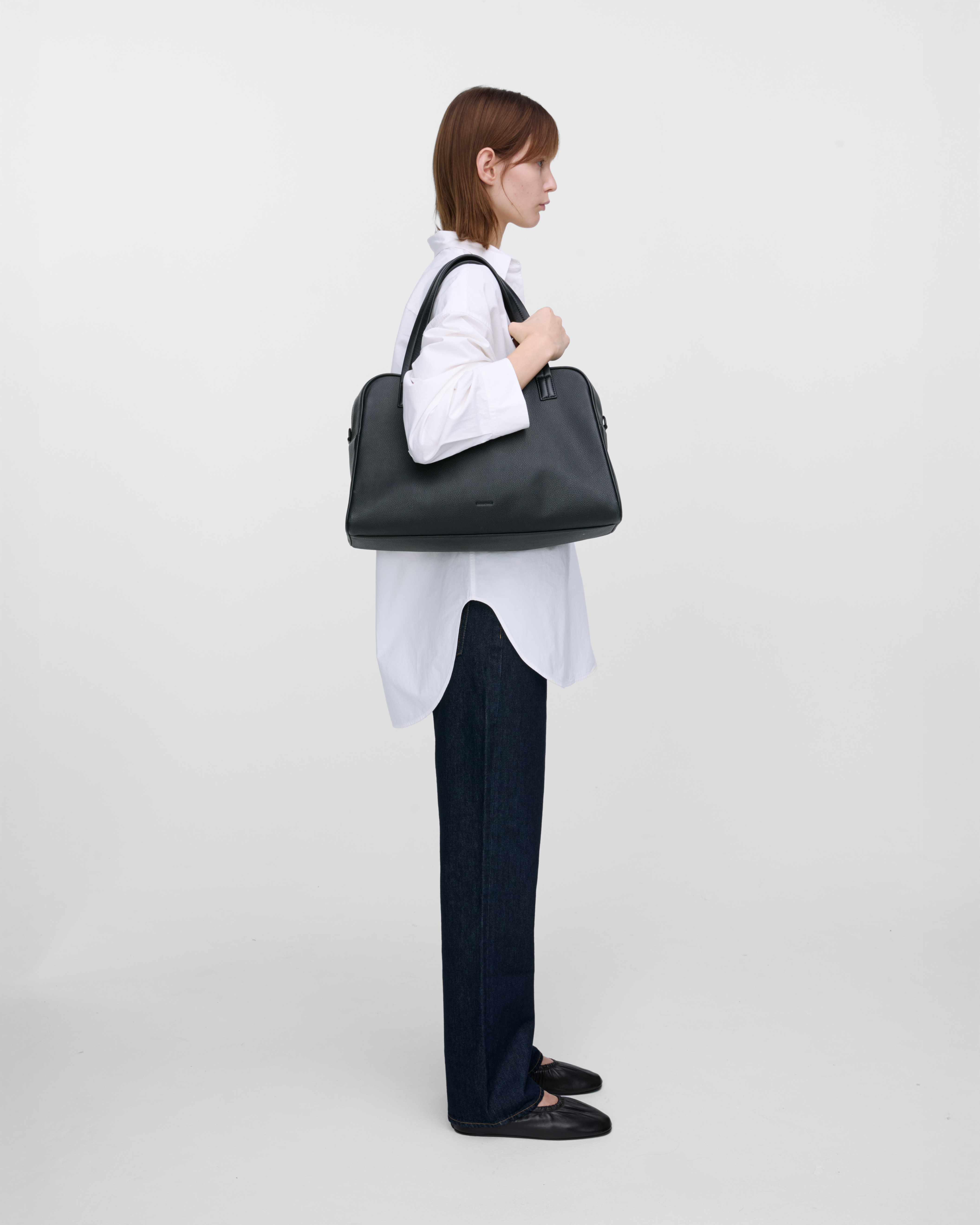 Female model carrying the handbag Sandqvist LEATHER Bowling Bag Black on the shoulder. Side view showing fit and size.