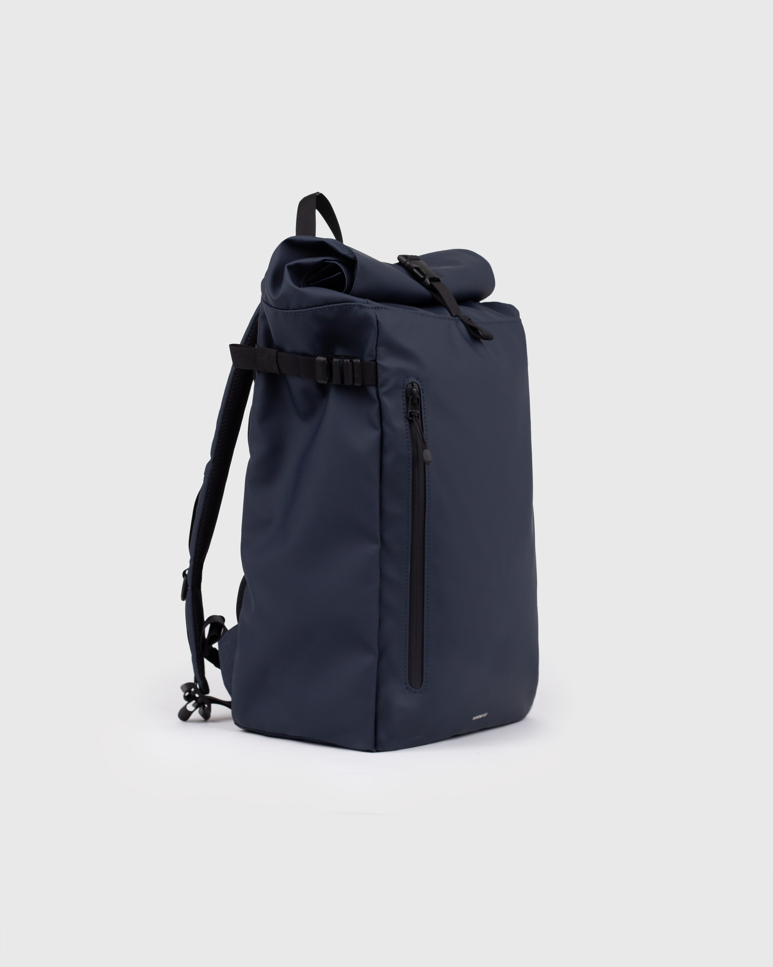 Sac à dos Sandqvist STREAM Slim Rolltop L bleu marine, vue latérale avec bandoulière, poignée supérieure, poche zippée à l'avant et fermeture à enroulement.