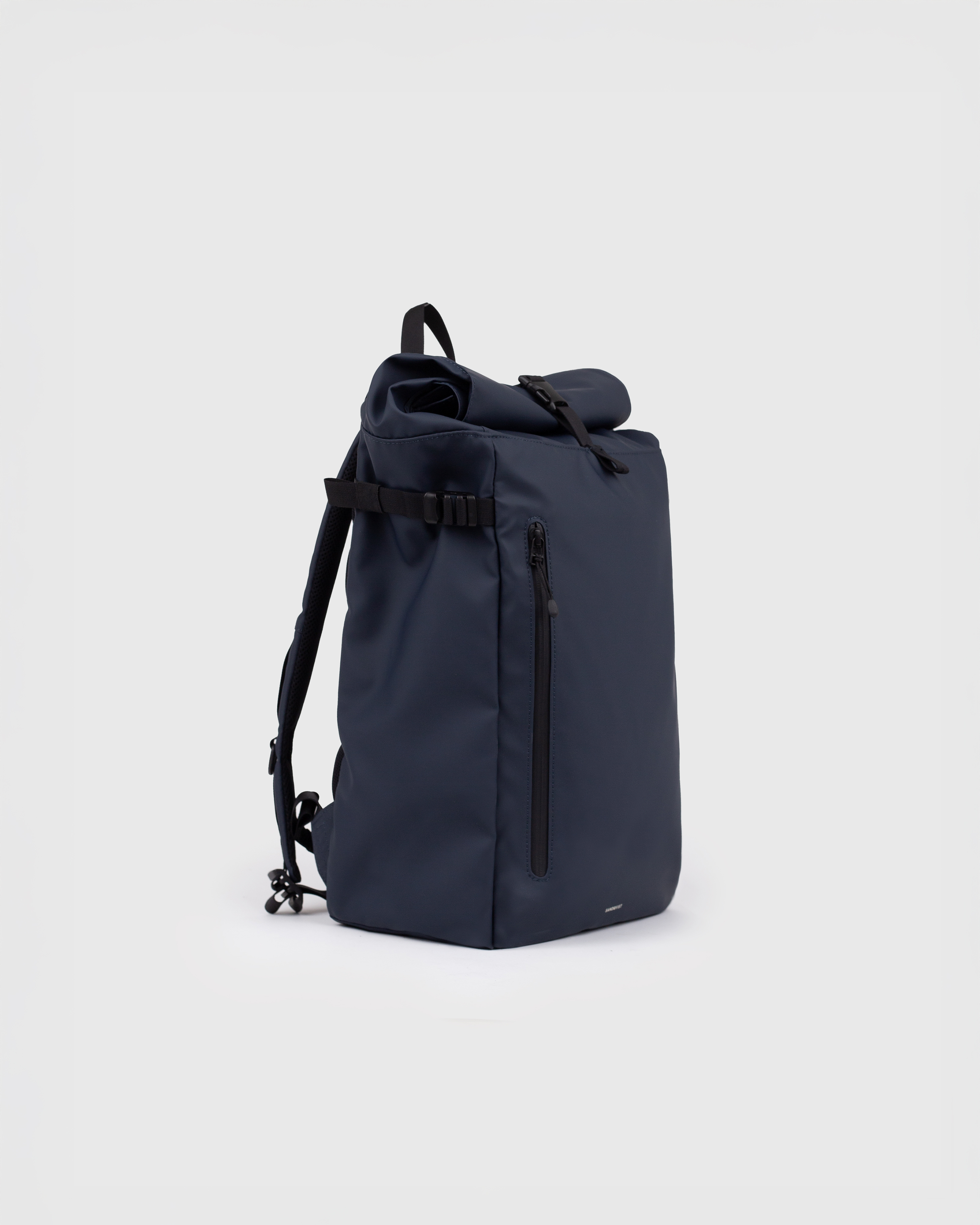 Sac à dos Sandqvist STREAM Slim Rolltop M bleu marine, vue latérale avec bandoulière, poignée supérieure, poche zippée à l'avant et fermeture à enroulement.