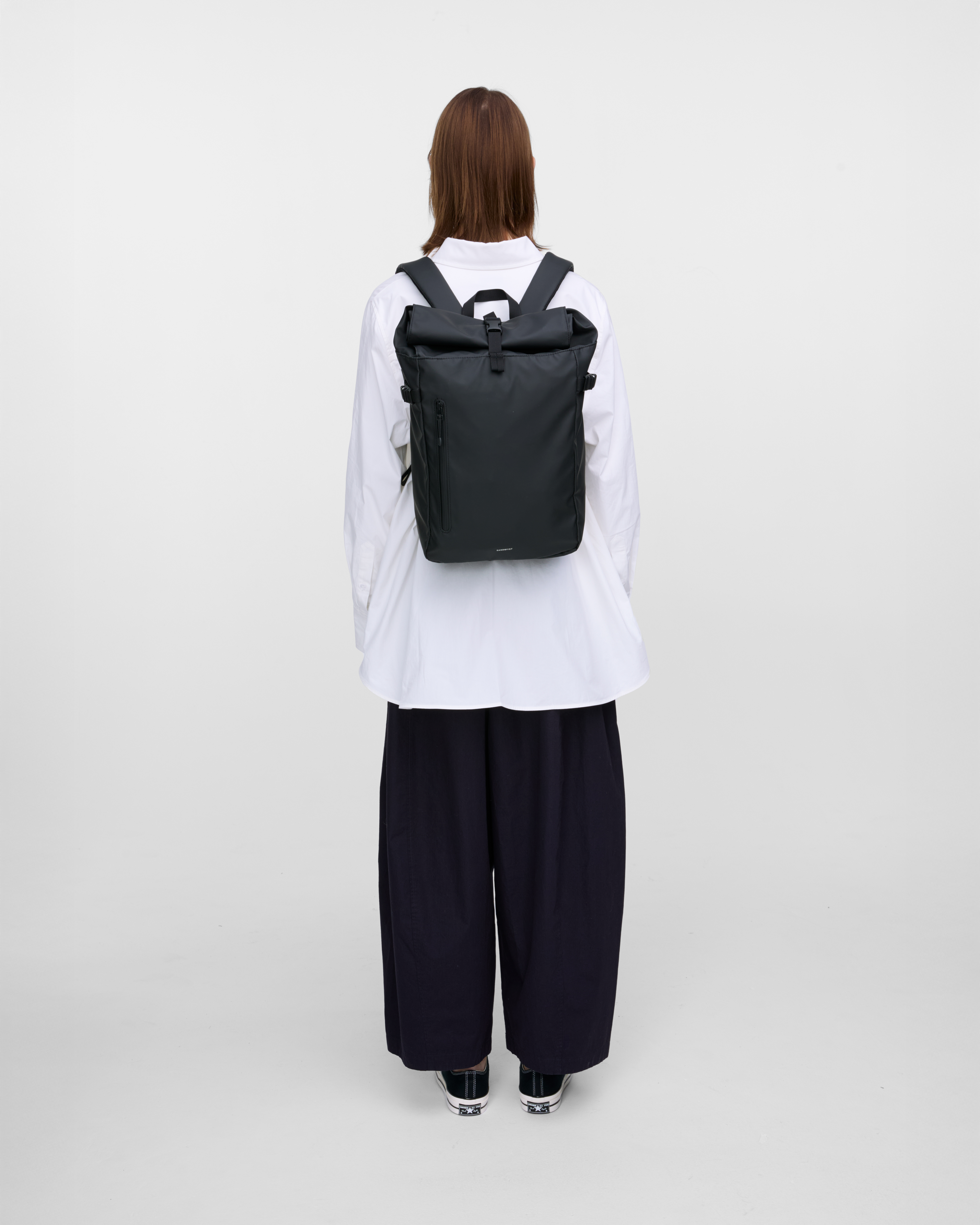  Female model carrying backpack STREAM Slim Rolltop M, Black, back view showing fit and size. 