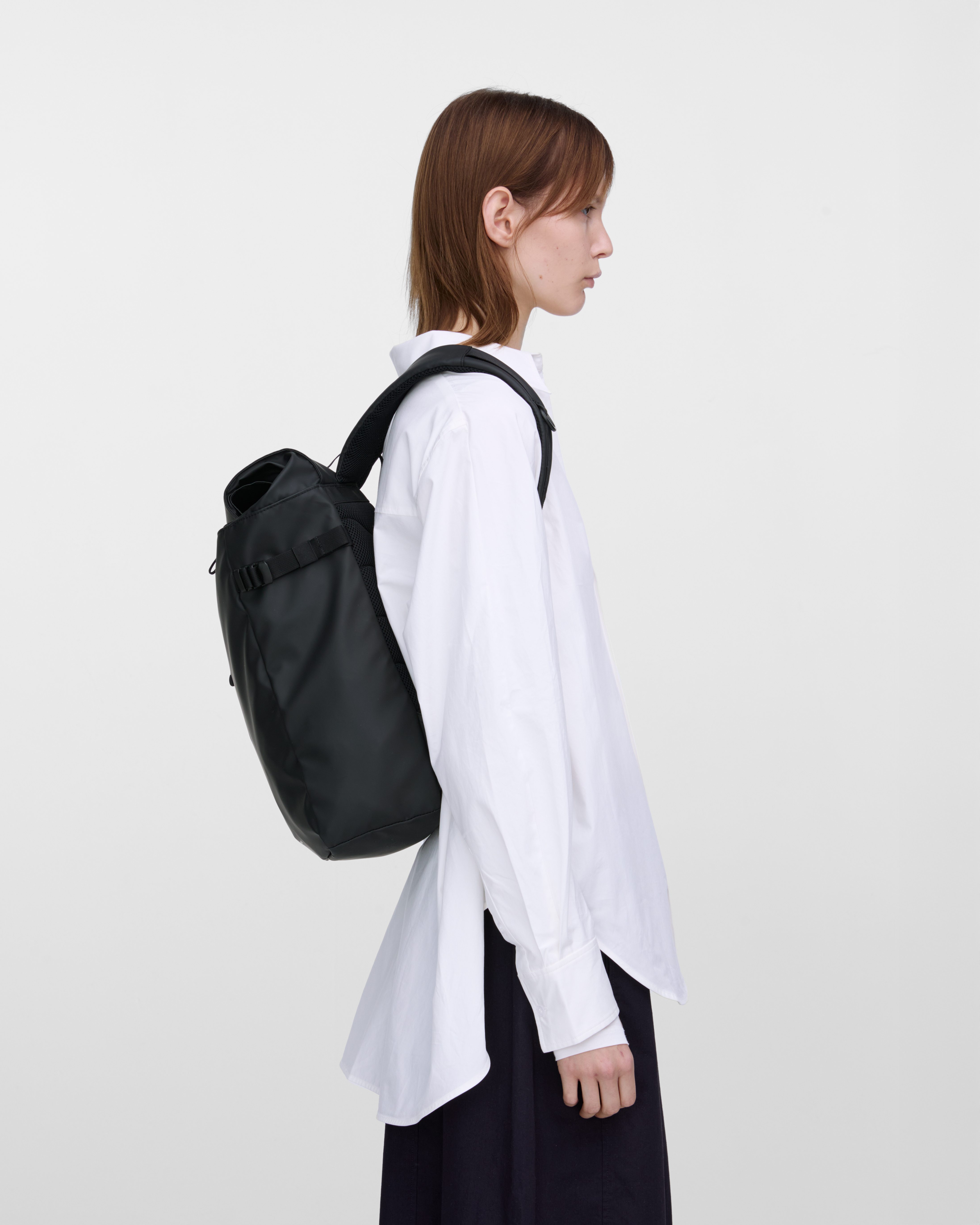 Female model carrying backpack STREAM Slim Rolltop M Black, side view showing fit and size. 