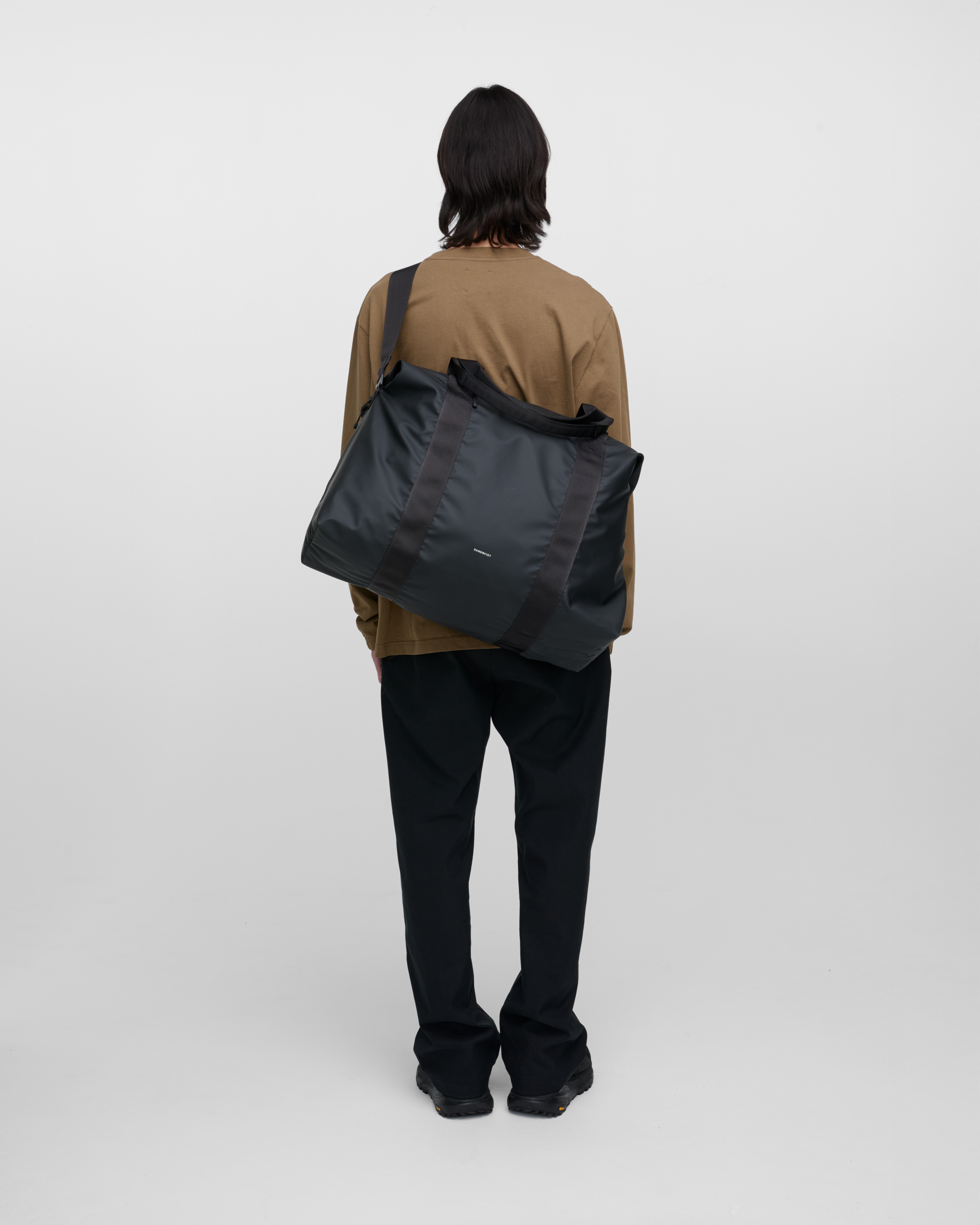 Male model wearing Sandqvist Weekender Bag, Black, back view carried on the shoulder over the back showing fit and size.