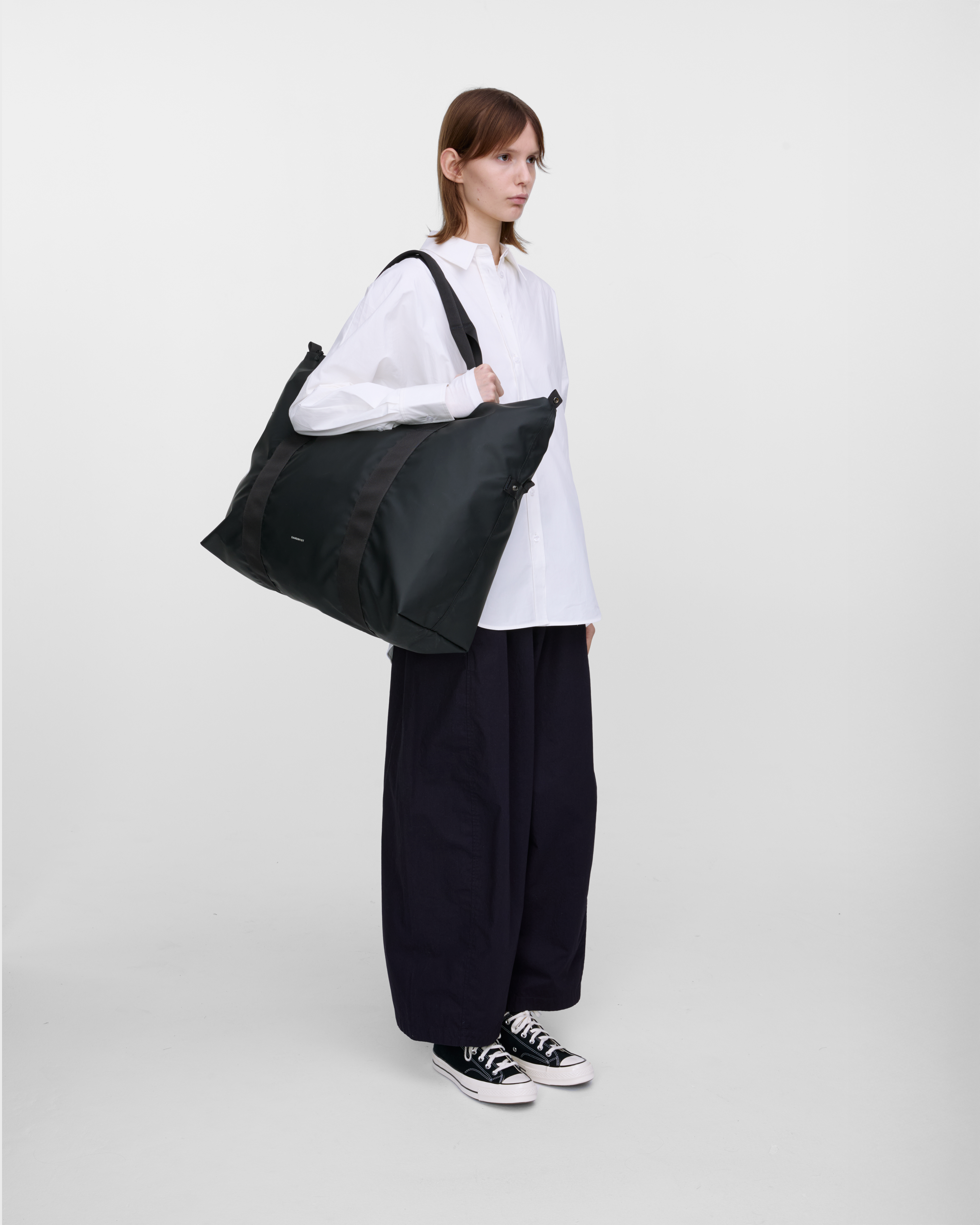 Female model wearing Sandqvist Weekender Bag, Black, side view carried on the shoulder showing fit and size.