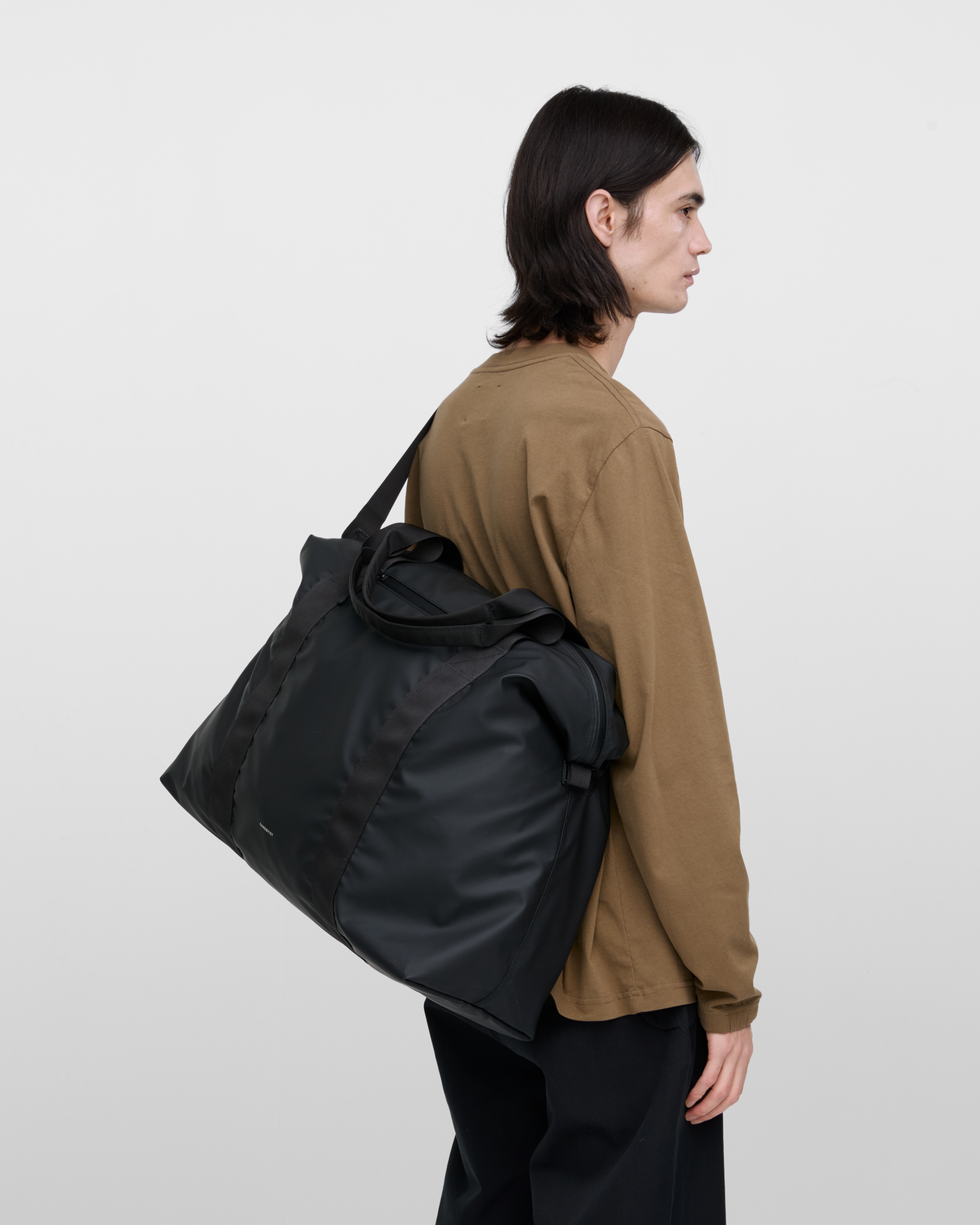 Male model wearing Sandqvist Weekender Bag, Black, view from the side showing fit and size hanging over the shoulder across the back.