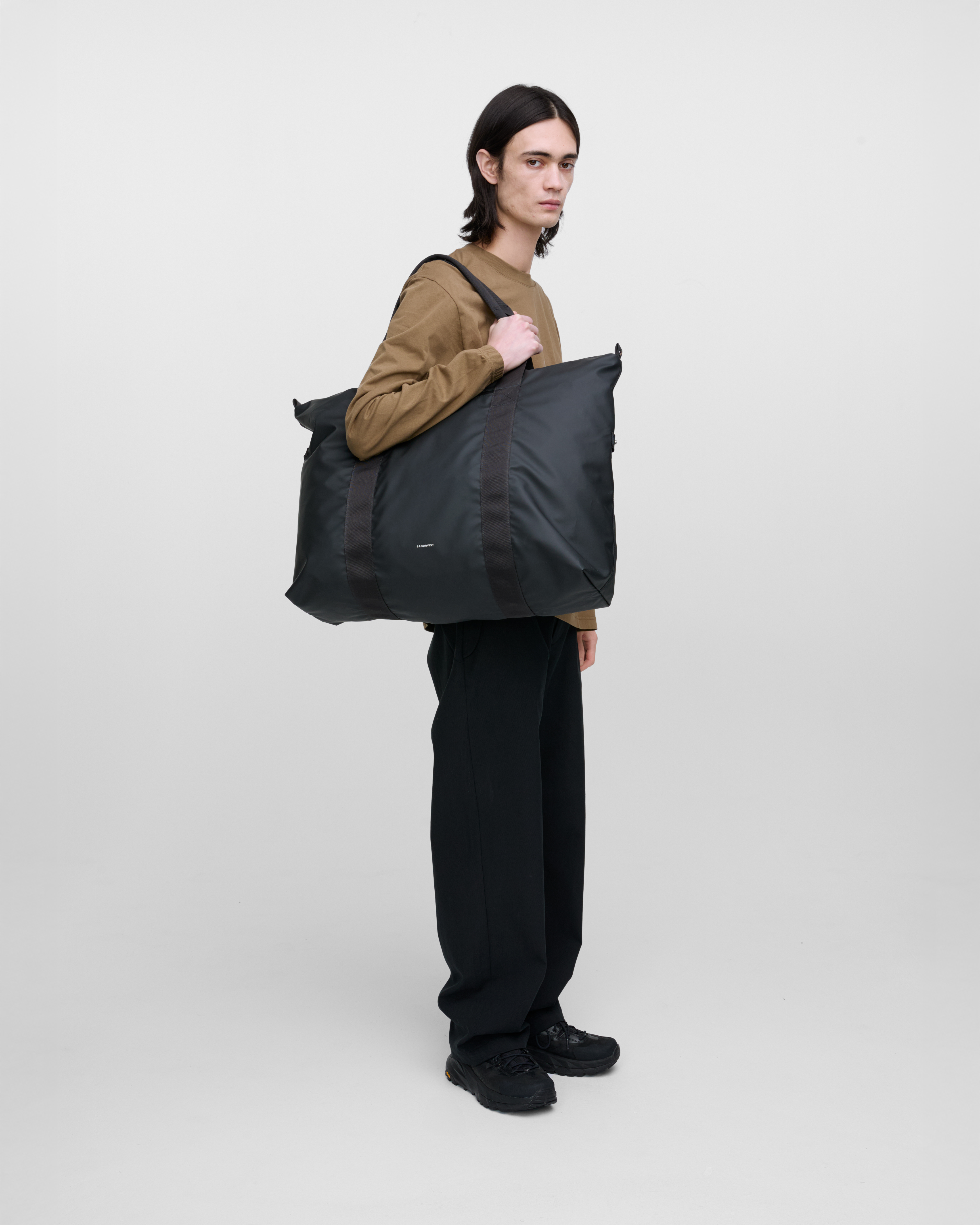 Male model wearing Sandqvist Weekender Bag, Black, side view carried on the shoulder showing fit and size.