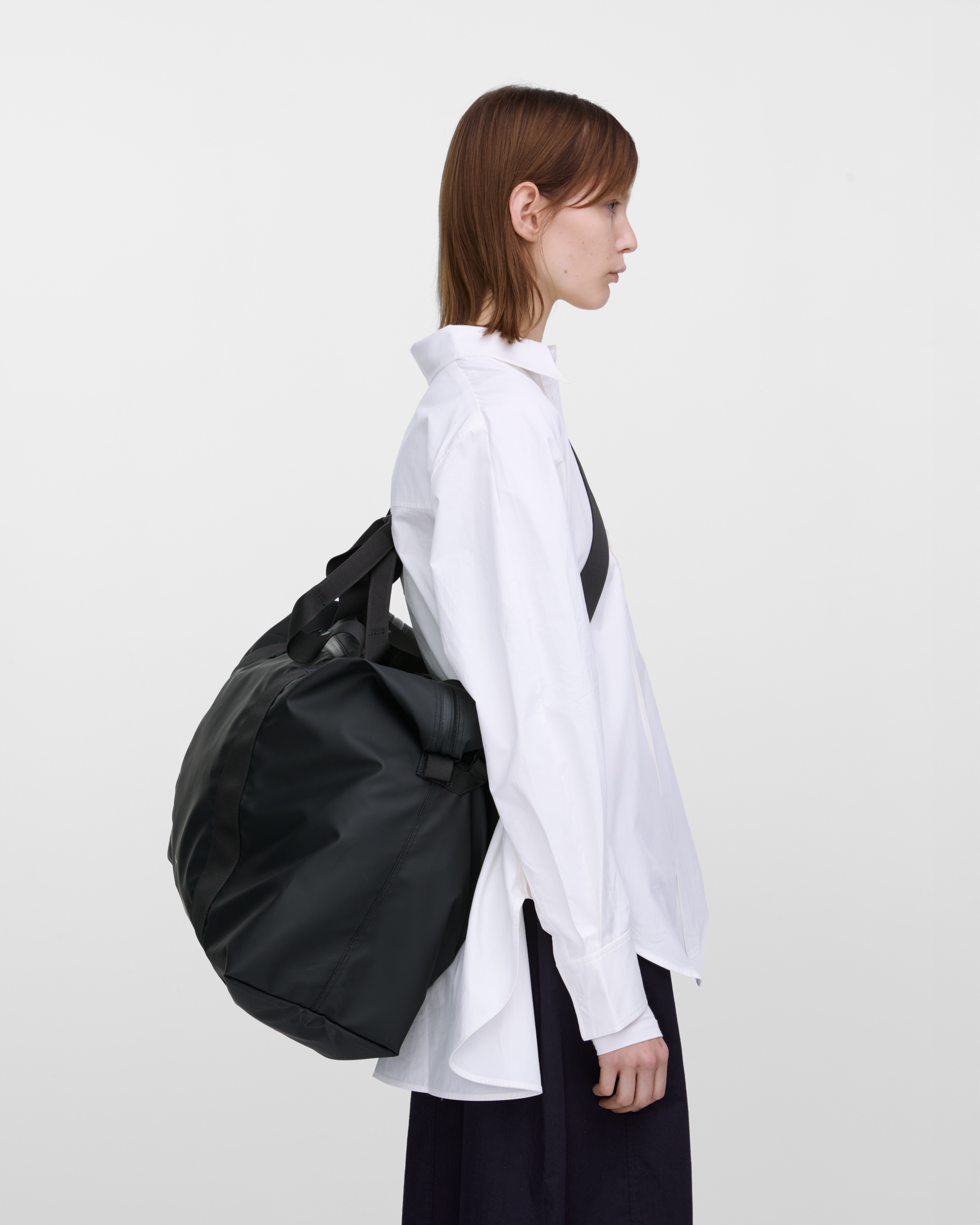 Female model wearing Sandqvist Weekender Bag, Black, view from the side showing fit and size hanging over the shoulder across the back.