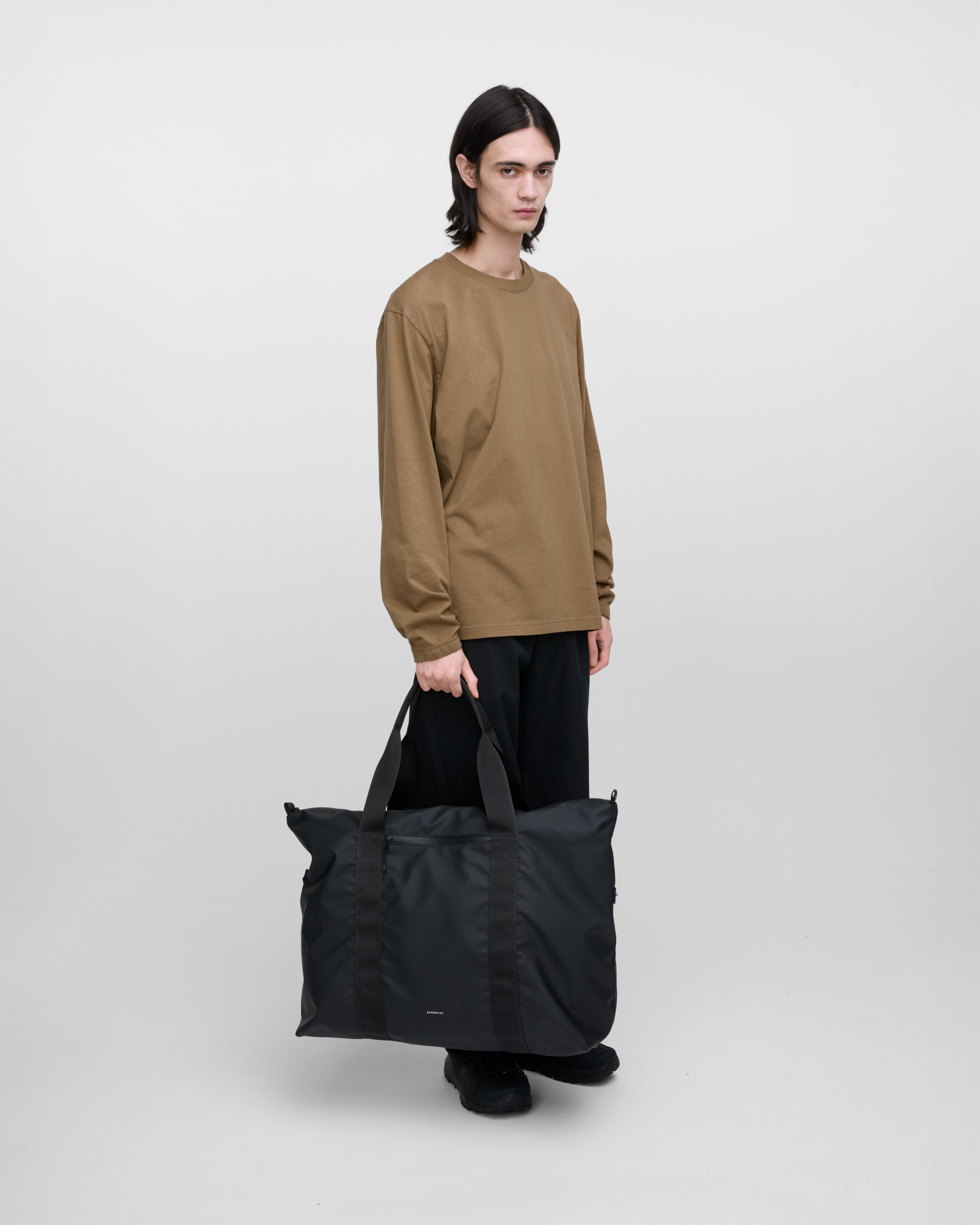Male model wearing Sandqvist Weekender Bag, Black, front view hand carrying, showing fit and size.