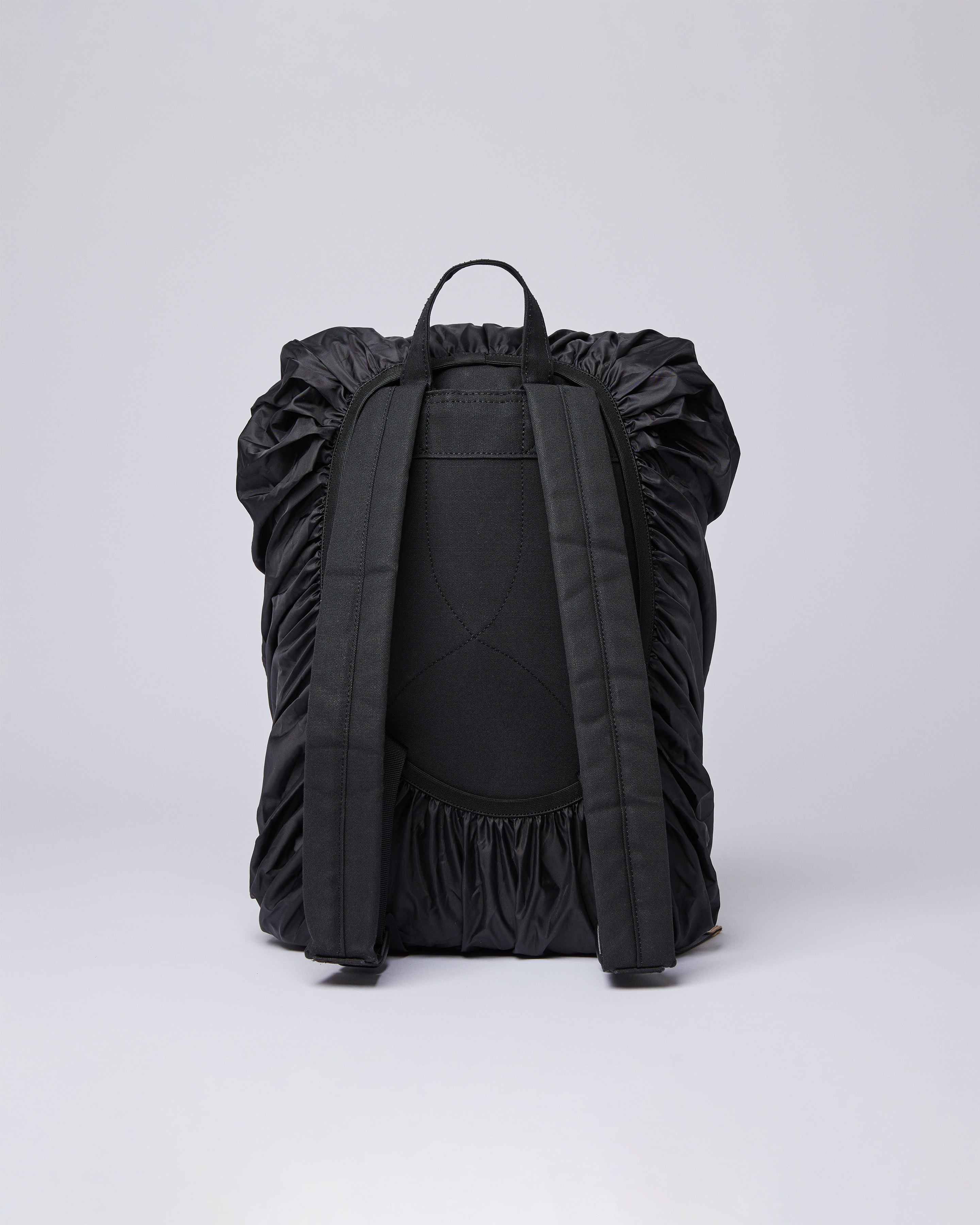Black backpack with rain cover on. Back view showing fit of Sandqvist ITEMS Backpack rain cover in black. 