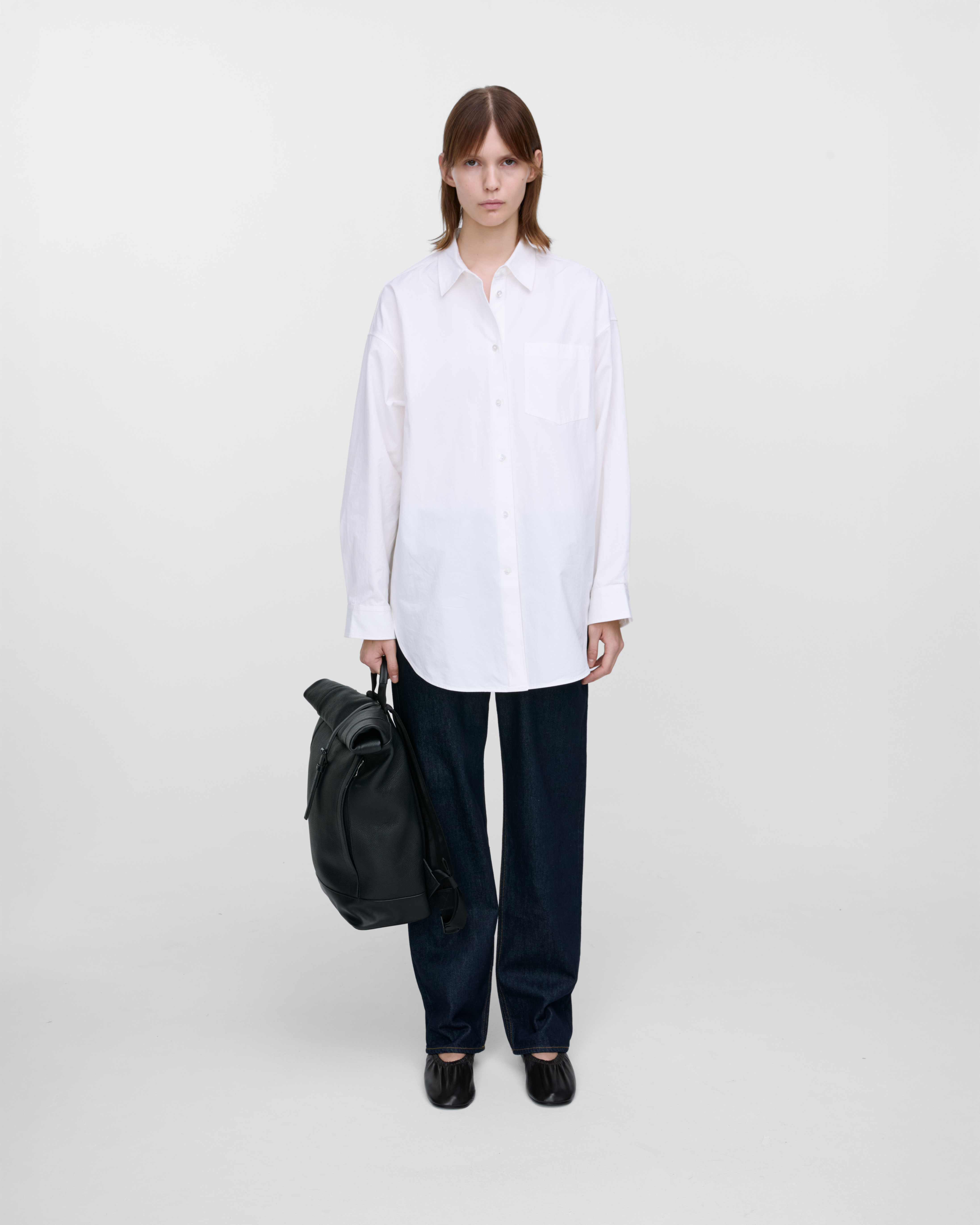 Female model carrying the backpack LEATHER Rolltop backpack black in hand, side view showing size.