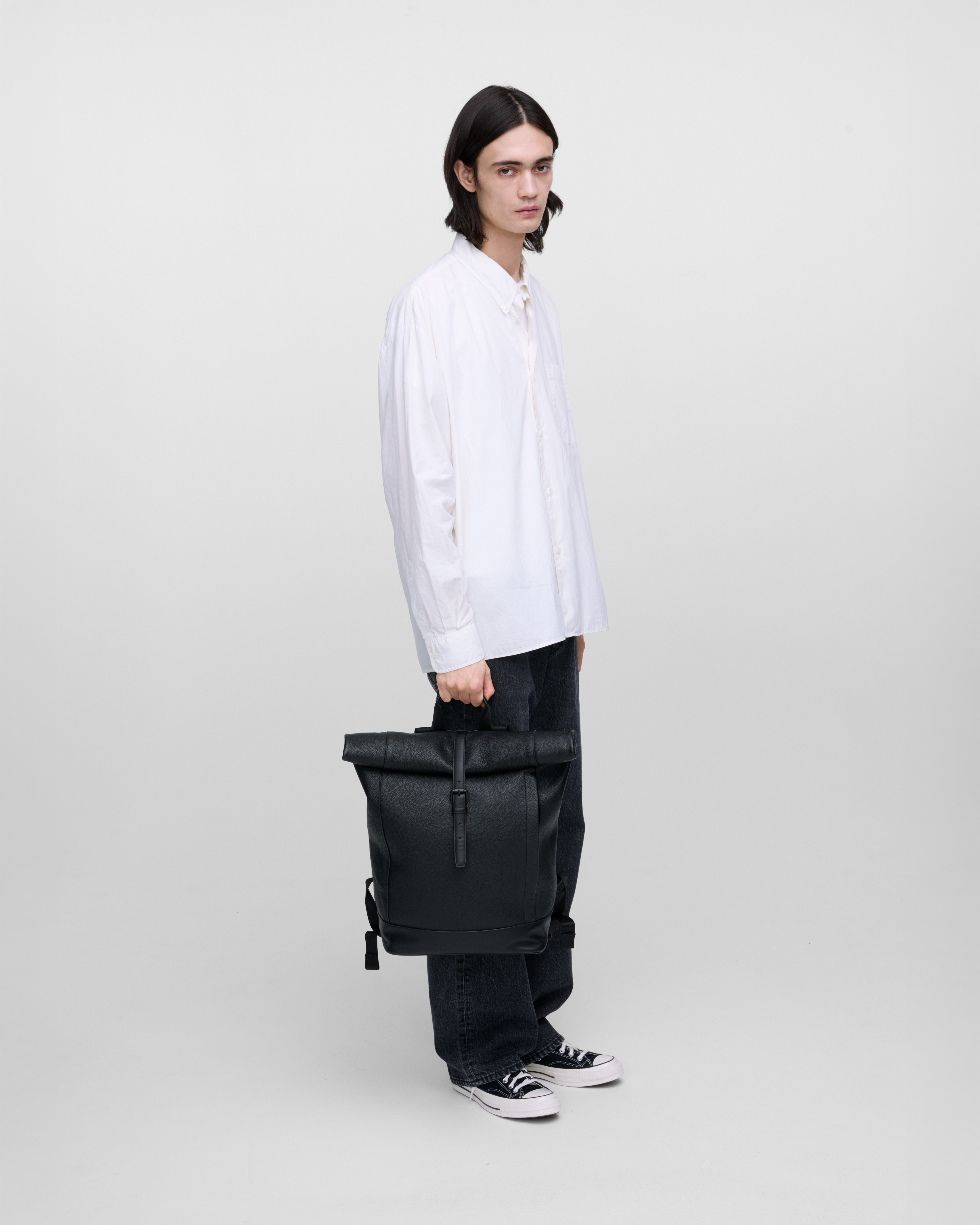 Male model carrying the backpack LEATHER Rolltop backpack black in hand, side view showing size.