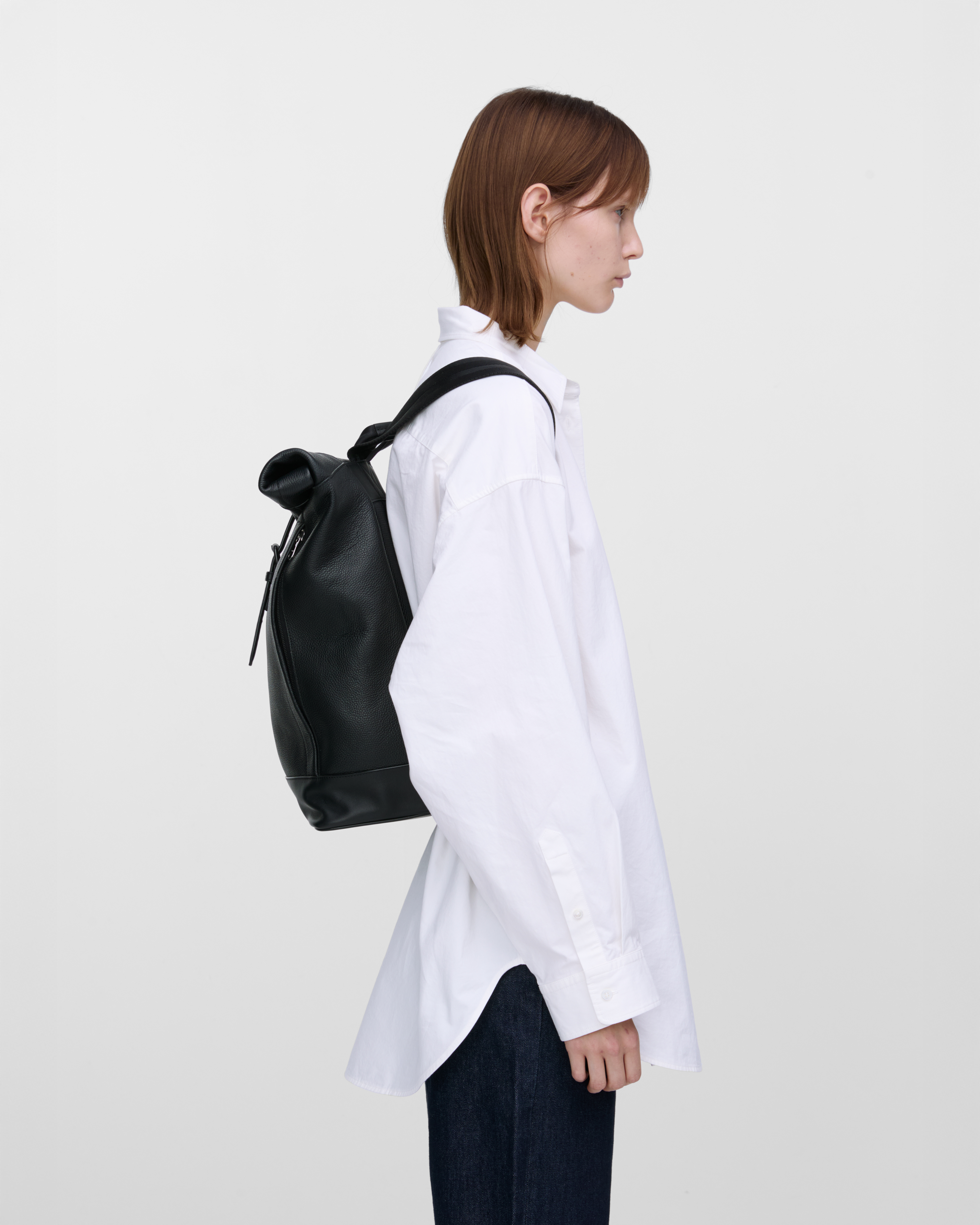 Female model carrying the backpack Sandqvist LEATHER Rolltop backpack in black. Side view showing fit and size.
