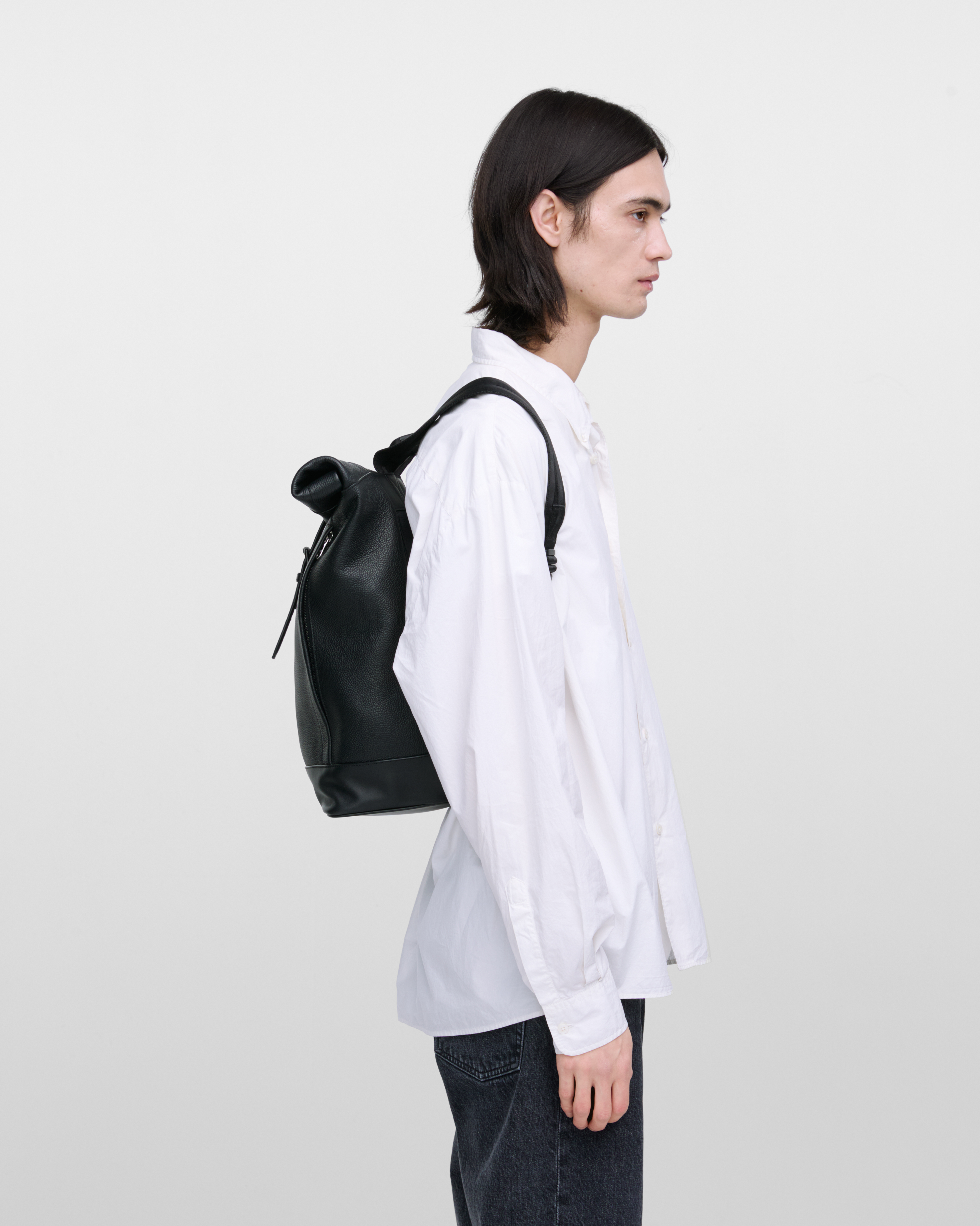 Male model carrying the backpack Sandqvist LEATHER Rolltop backpack in black. Side view showing fit and size.