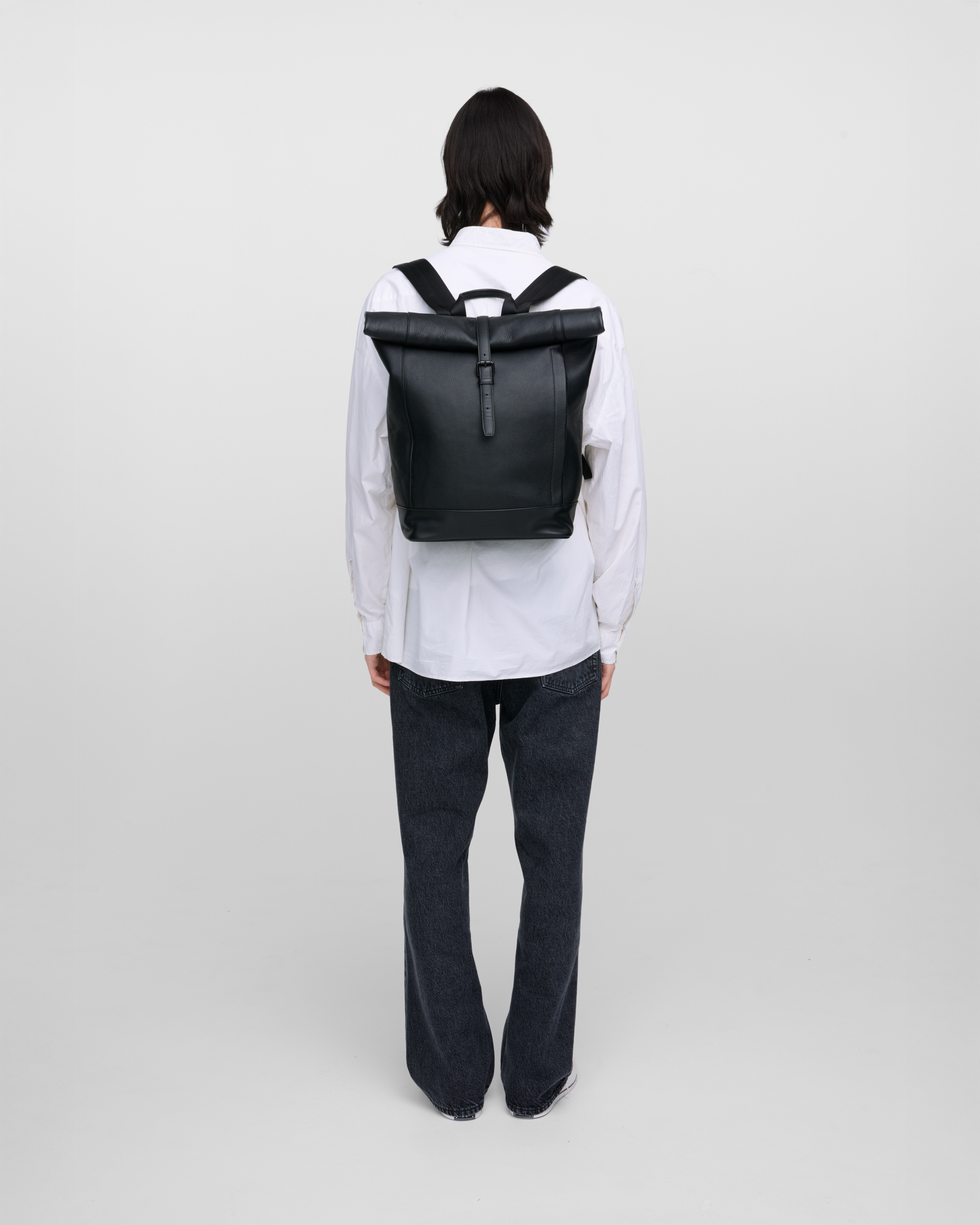 Male model carrying the backpack Sandqvist LEATHER Rolltop backpack in black. Back view showing fit and size.