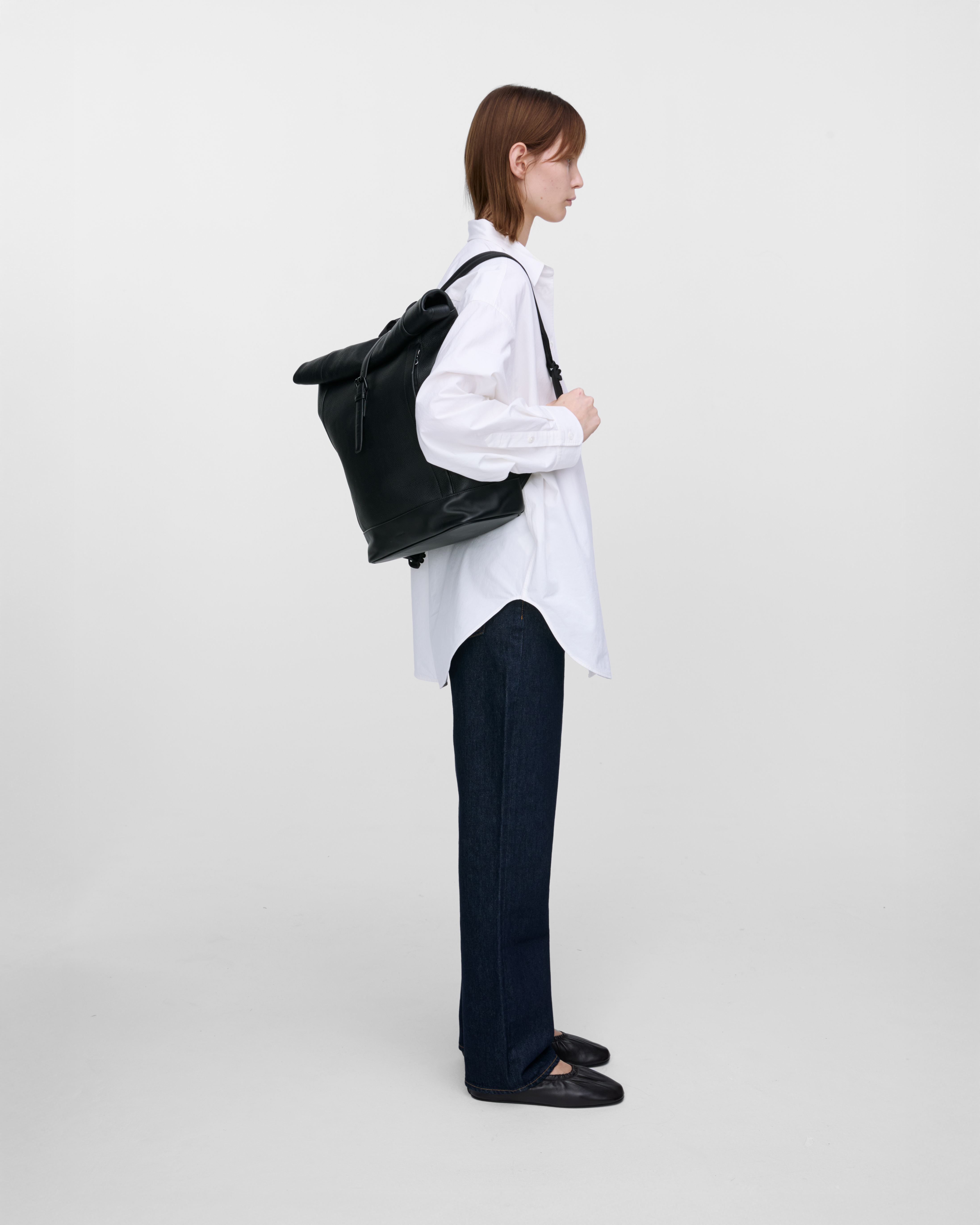 Female model carrying the backpack Sandqvist LEATHER Rolltop backpack, Black, hanging over one shoulder, side view showing fit and size.