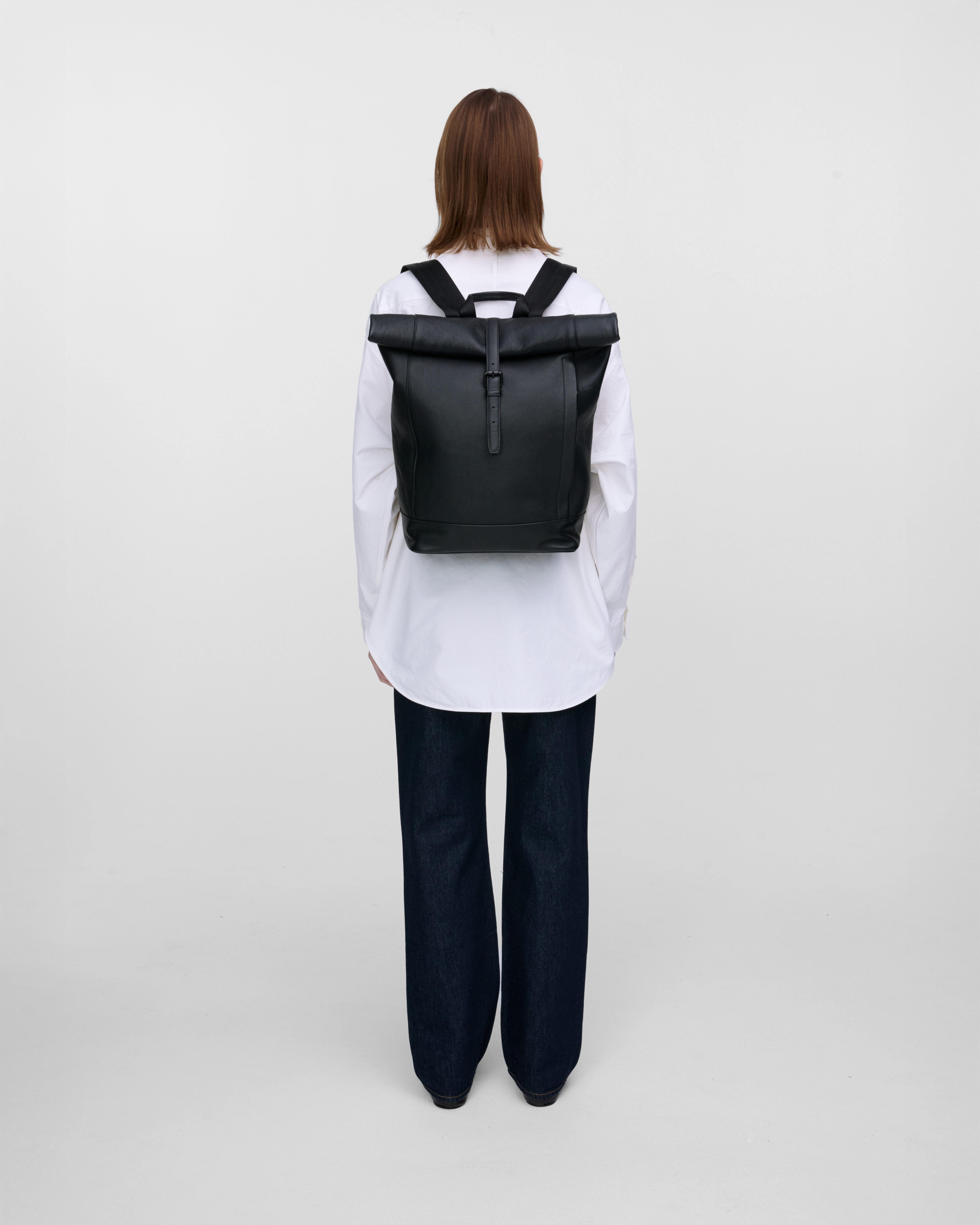 Female model carrying the backpack Sandqvist LEATHER Rolltop backpack in black. Back view showing fit and size. 