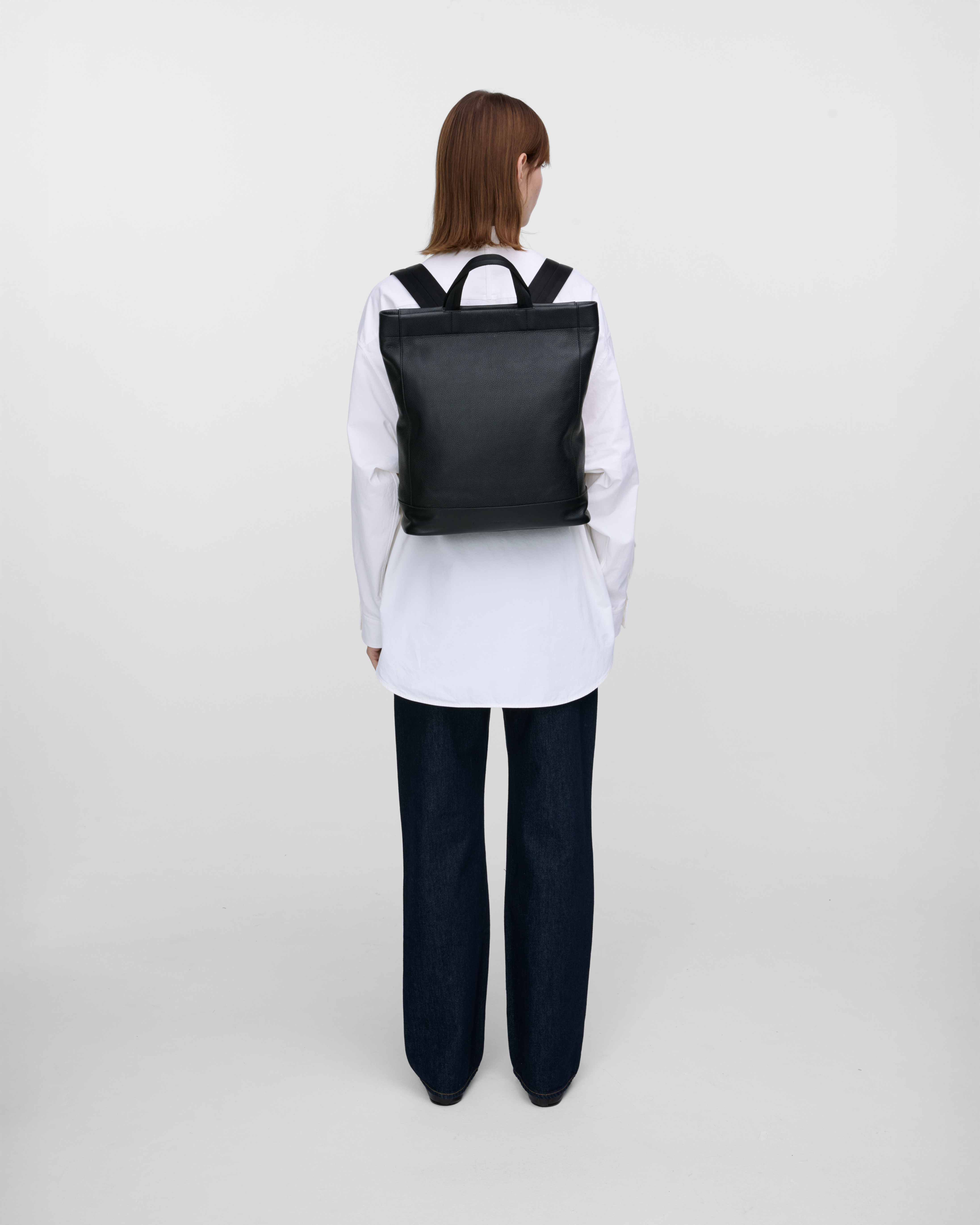 Female model carrying backpack Sandqvist LEATHER Tote Backpack, Black, back view showing fit and size. 