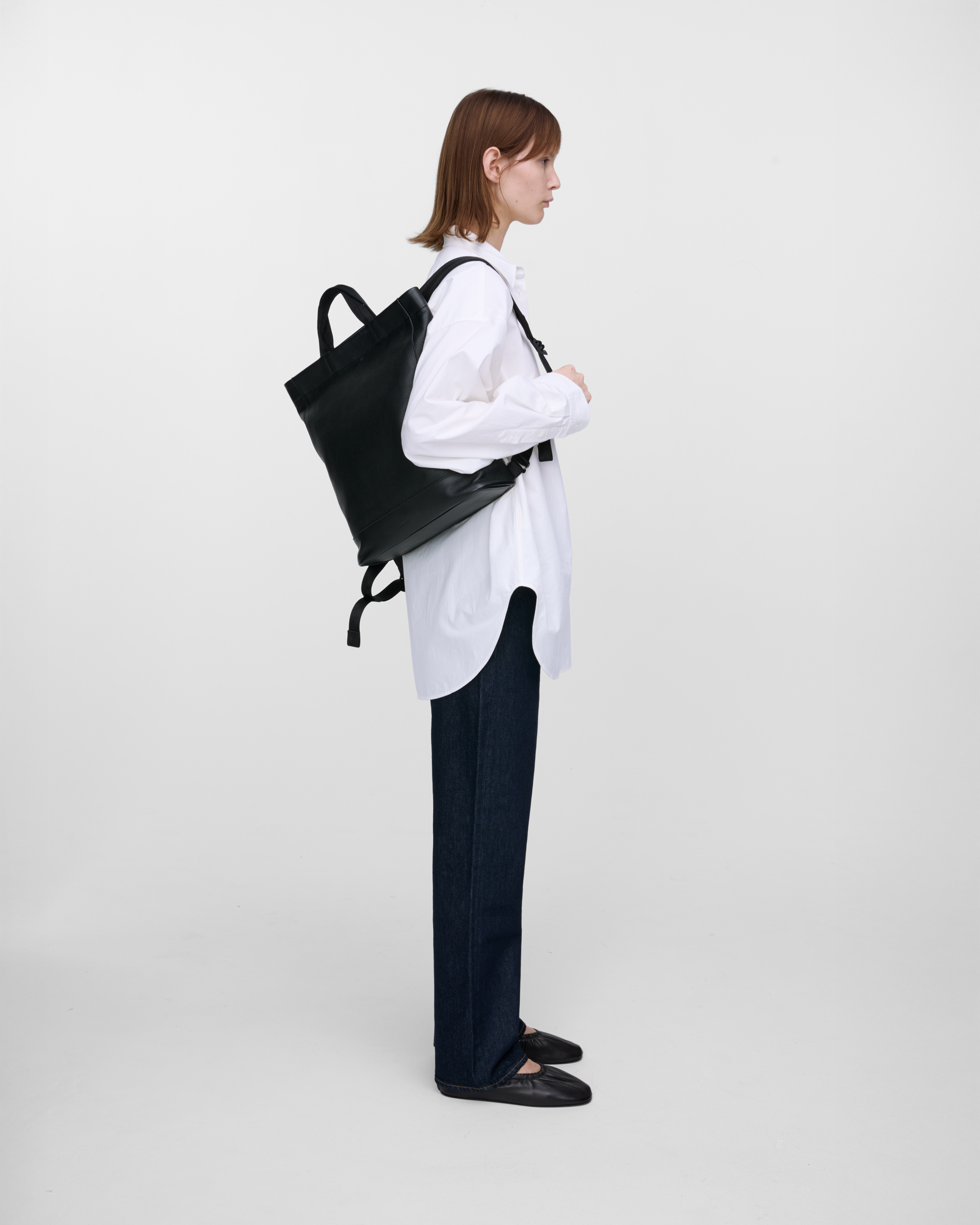Female model carrying backpack Sandqvist LEATHER Tote Backpack, Black, hanging over one shoulder, back view showing fit and size. 