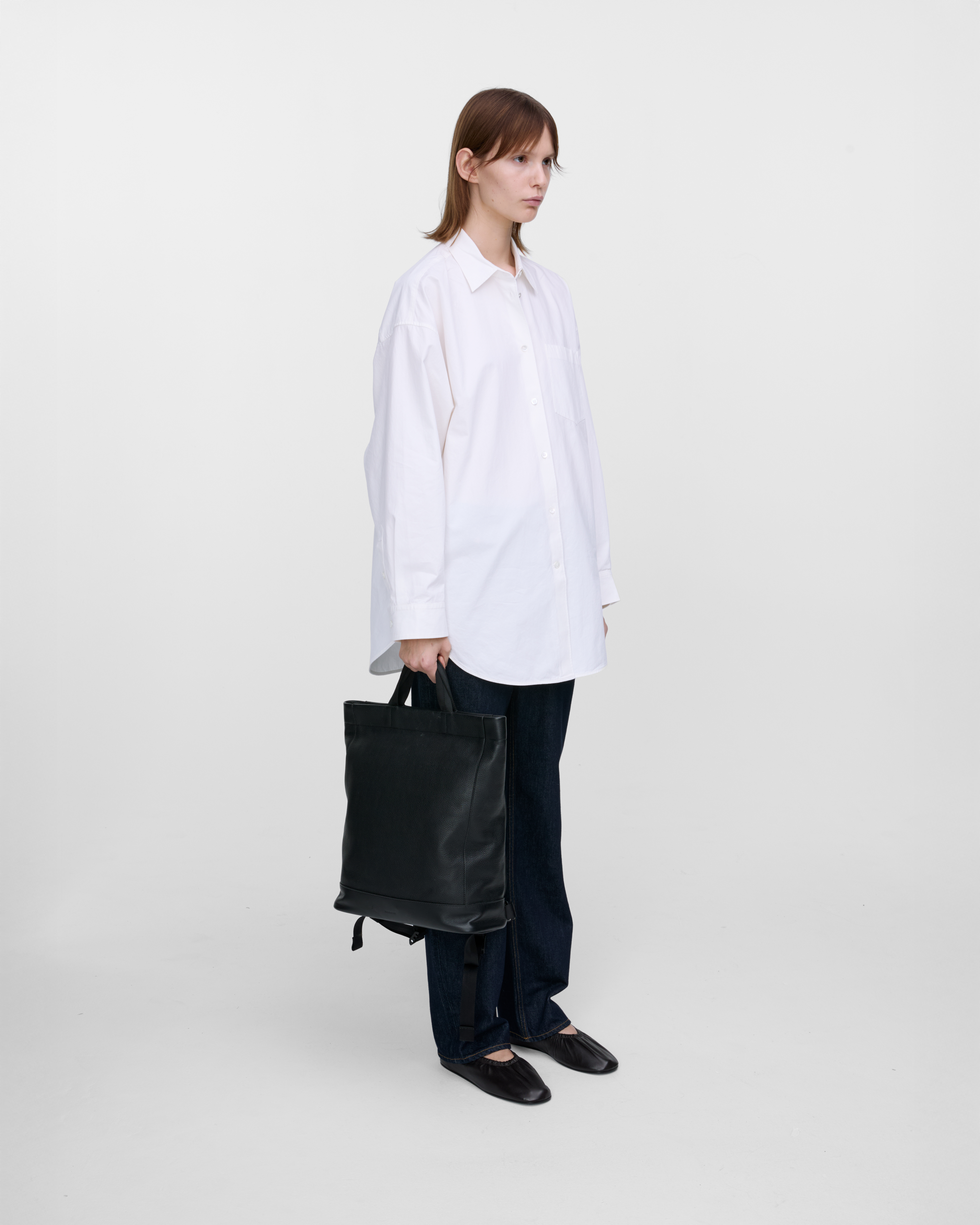 Female model carrying the backpack Sandqvist LEATHER Tote Backpack Black in hand, side view showing size. 