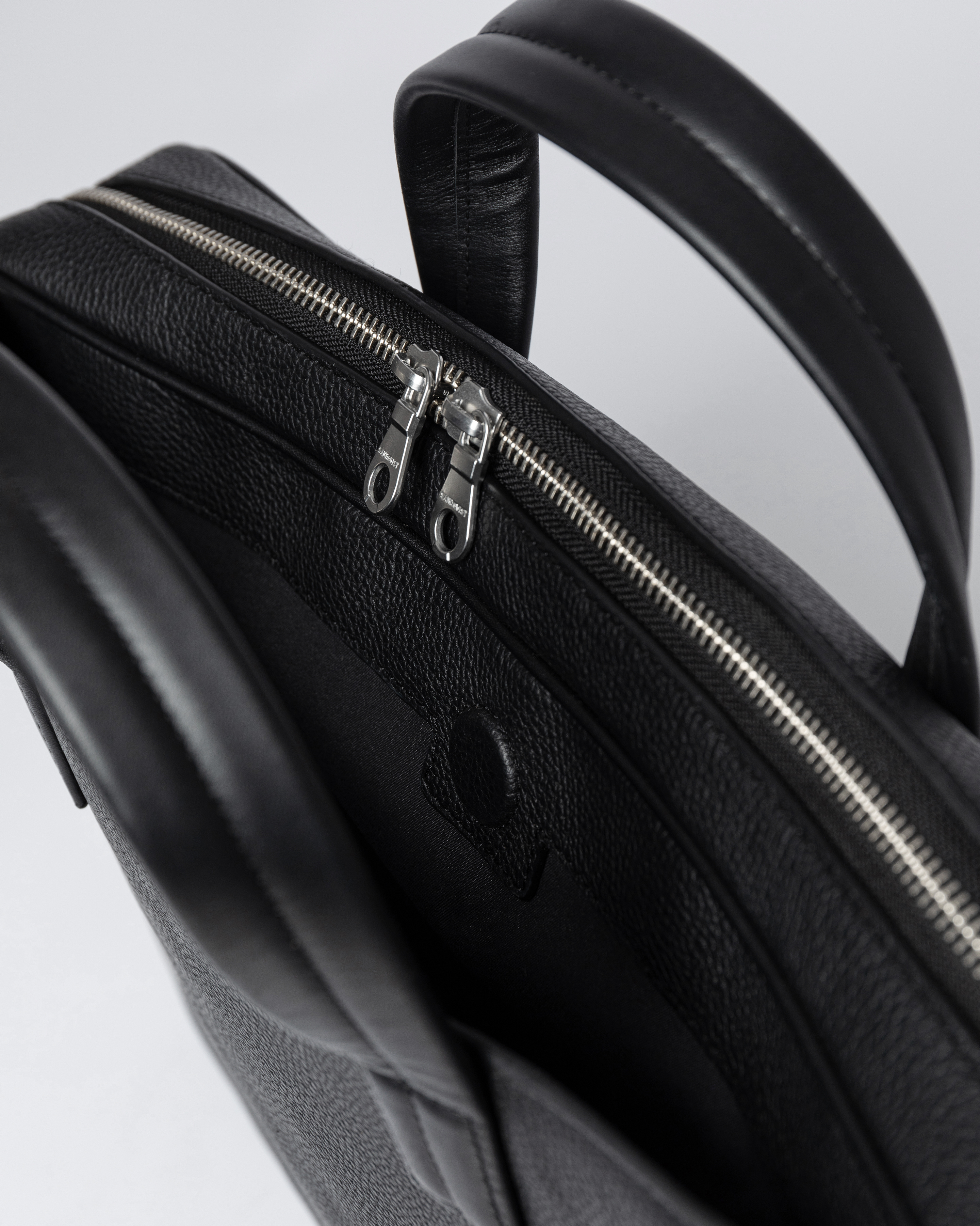 Closed zipper compartment and internal laptop pocket with strap and press button in the Sandqvist LEATHER Briefcase black.