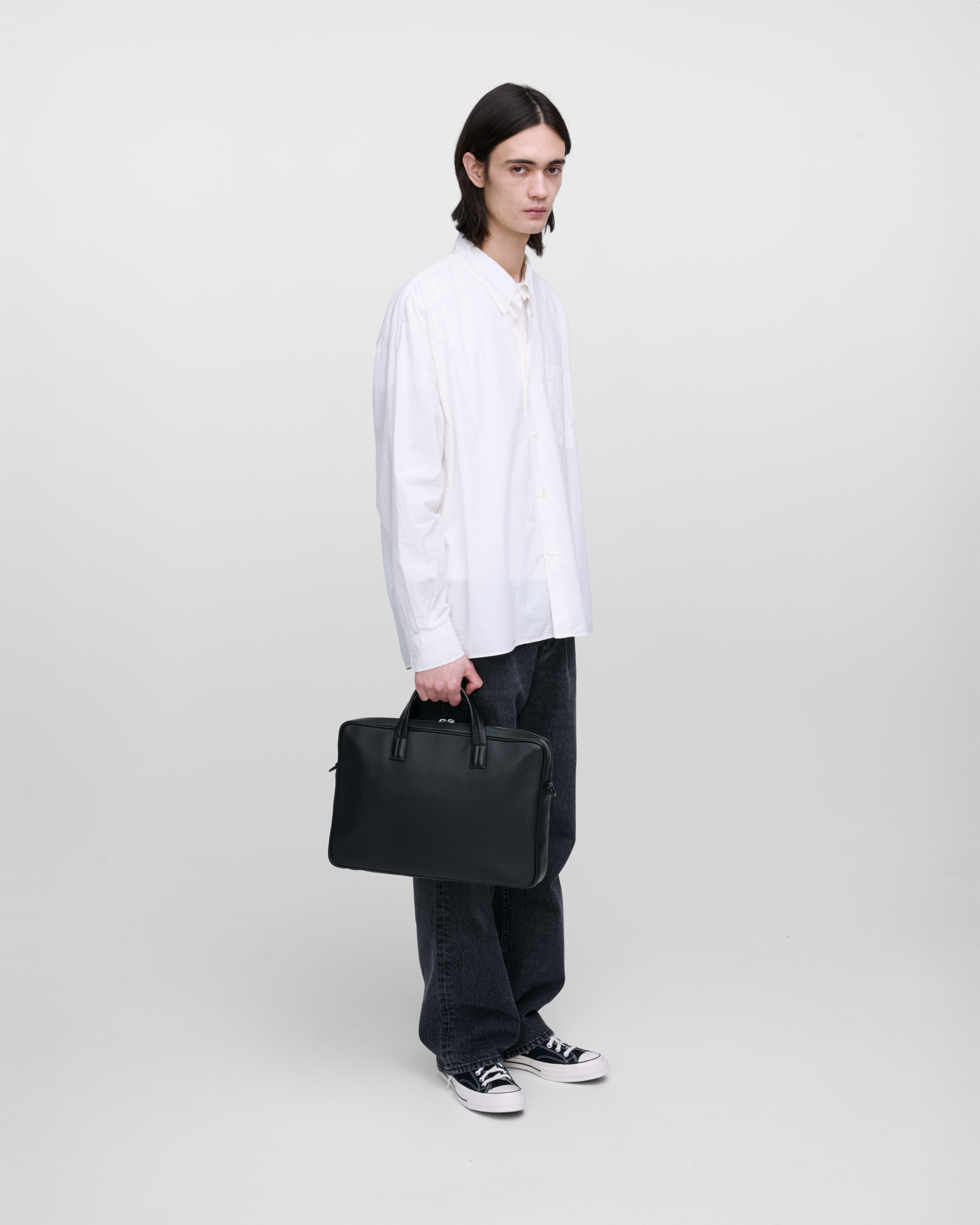 Male model holding the briefcase Sandqvist LEATHER Briefcase Black in the hand, side view showing fit and size.