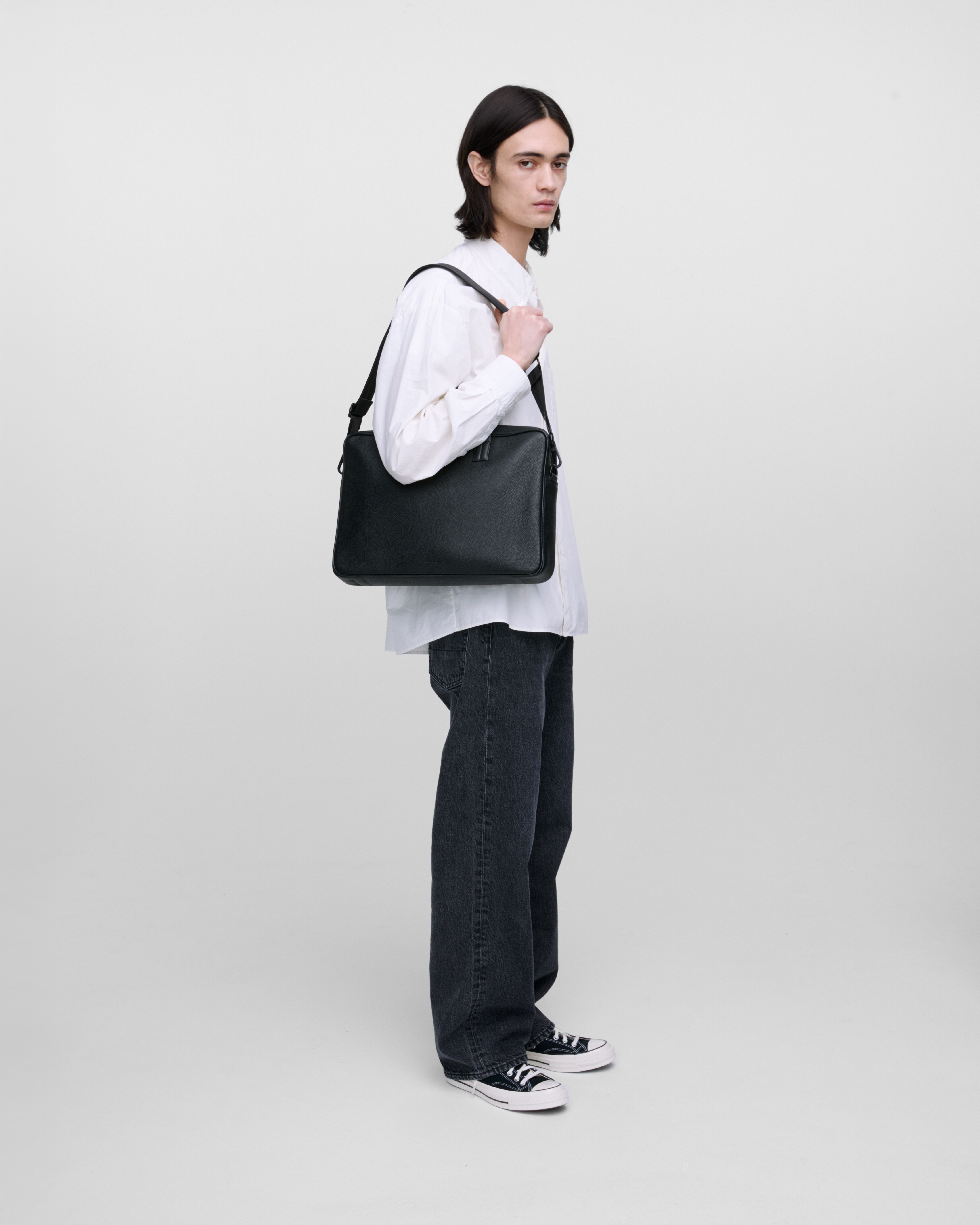 Male model carrying the briefcase Sandqvist LEATHER Briefcase Blackon the shoulder, side view showing fit and size.