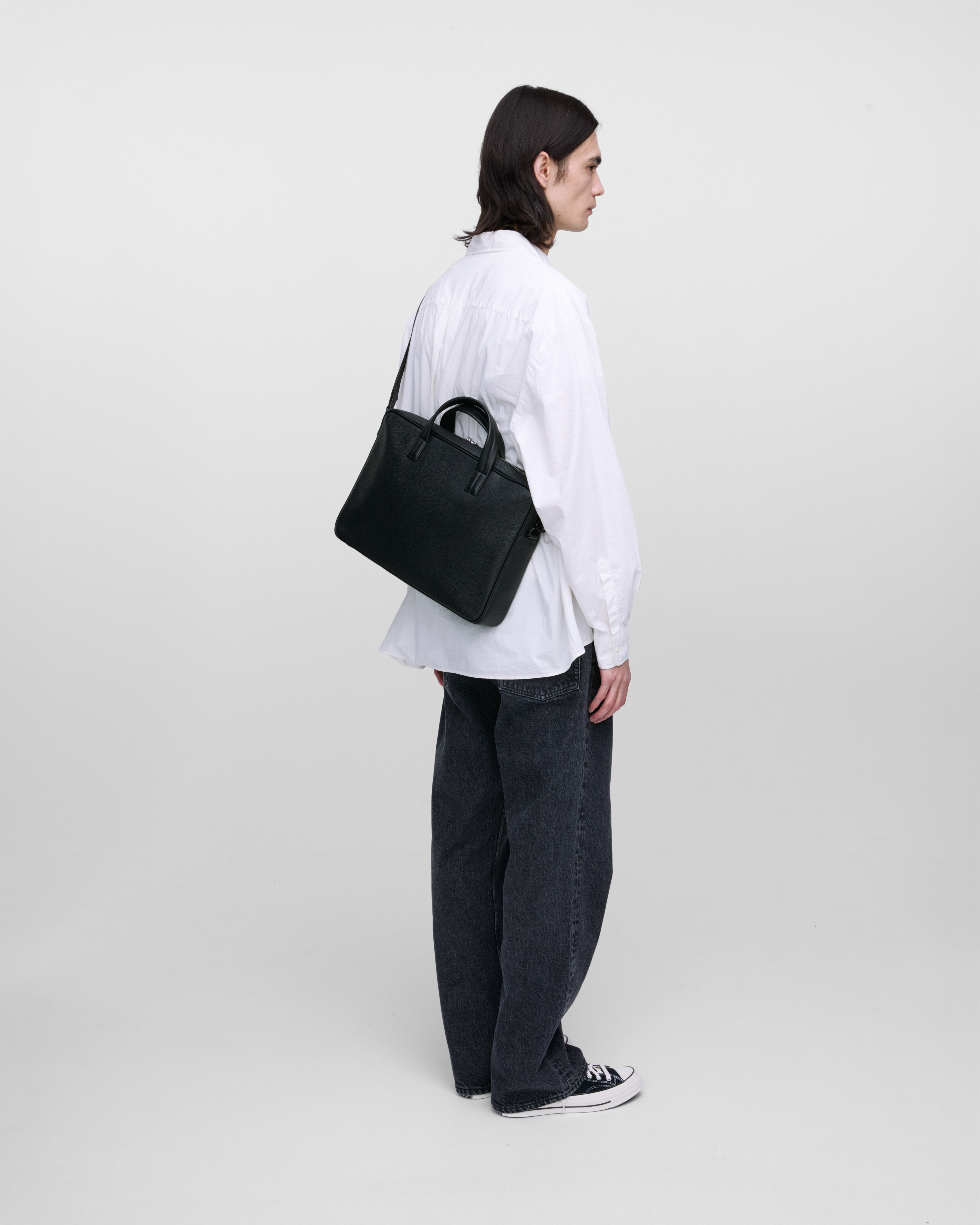 Male model wearing the briefcase Sandqvist LEATHER Briefcase in Black, side view carried on the shoulder showing fit and size.