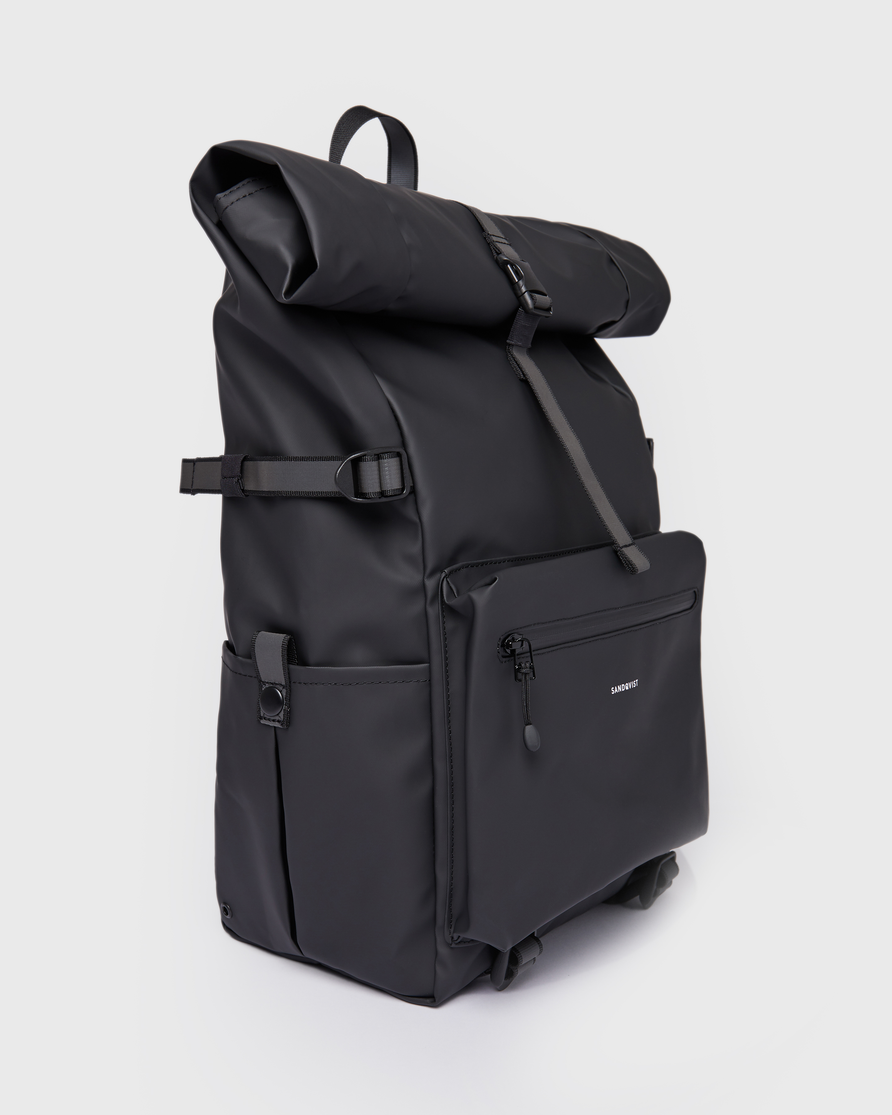 Sandqvist Backpack Ruben 2.0 in Black. Side view with reflective side strap, side slip pocket, front zipper pocket and rolltop closure.