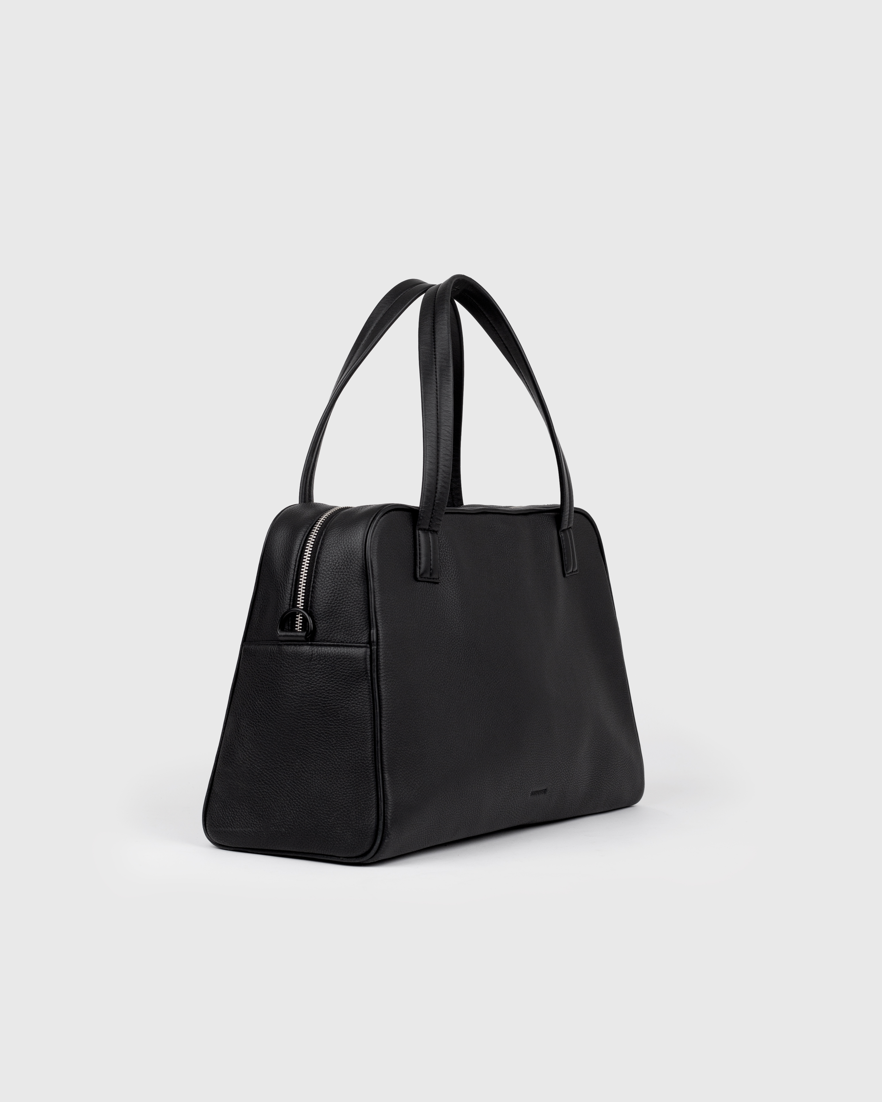 Handbag in leather. Sandqvist LEATHER Bowling Bag in Black, side view with two top handles and zippered main compartment.