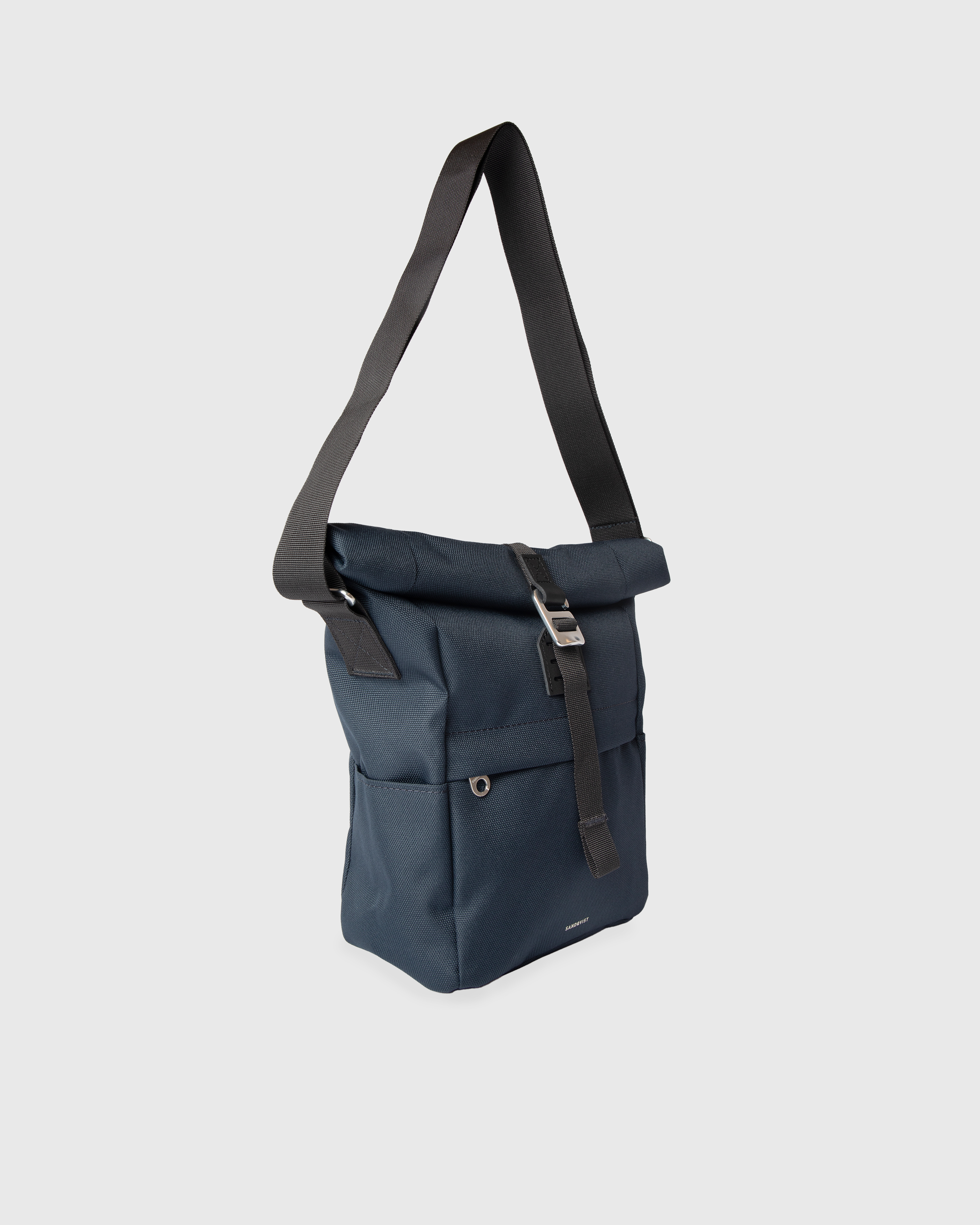 Sandqvist ICON Sacoche in navy, side view with shoulder strap, rolltop closure, side slip pocket and front zipper pocket.