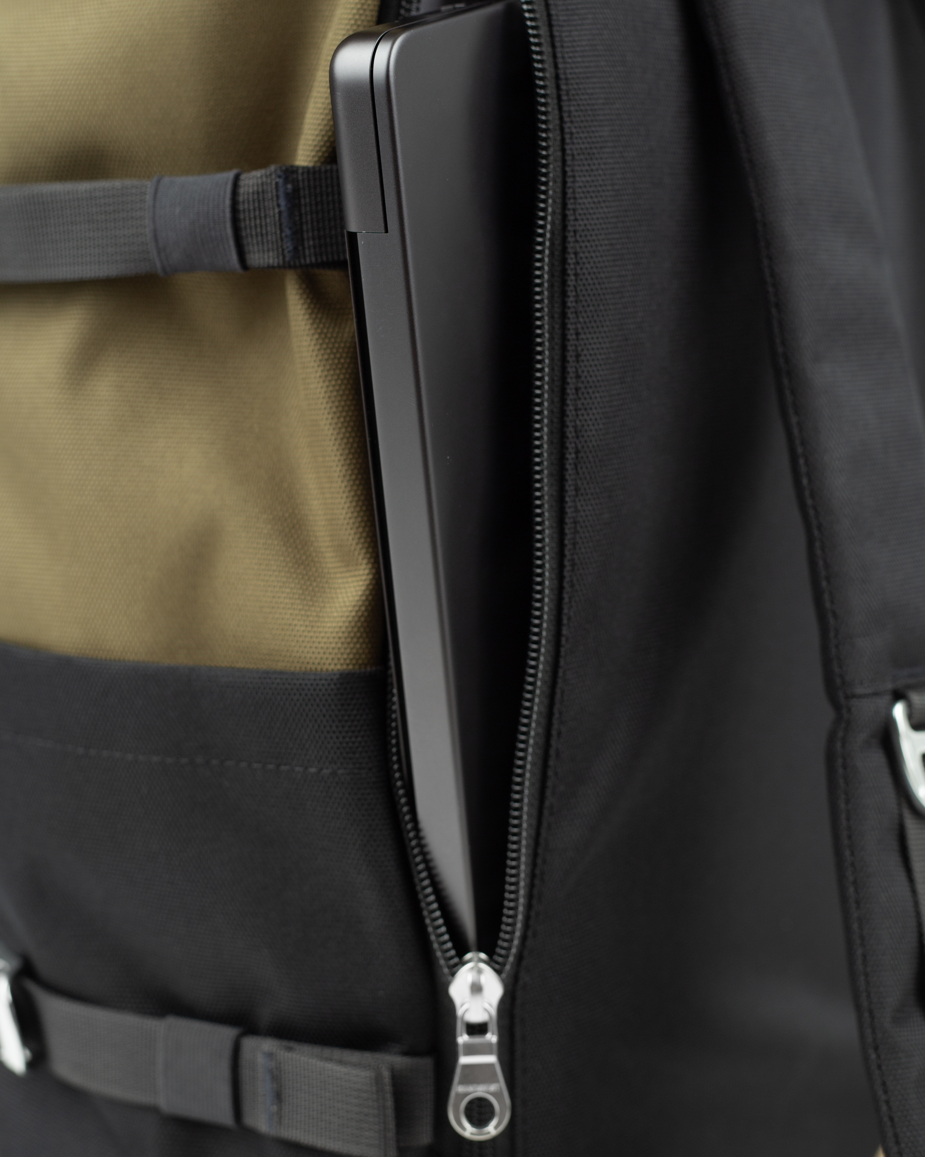 Sandqvist Icon Rolltop Rucksack L 16, grün und schwarz. Nahaufnahme des äußeren Laptopfachs mit Reißverschluss.